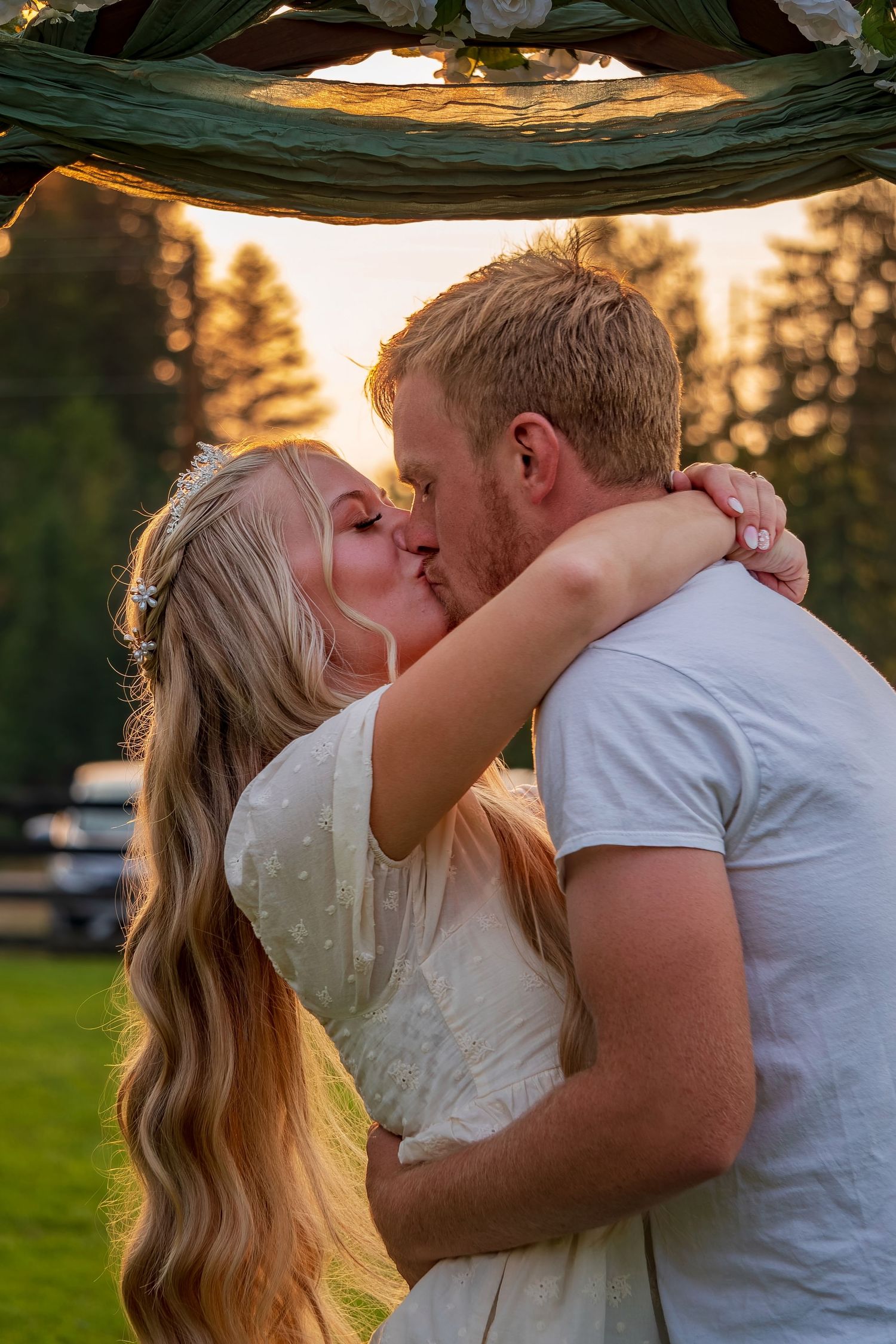 Romantic kiss under decorated arch during sunset wedding ceremony.