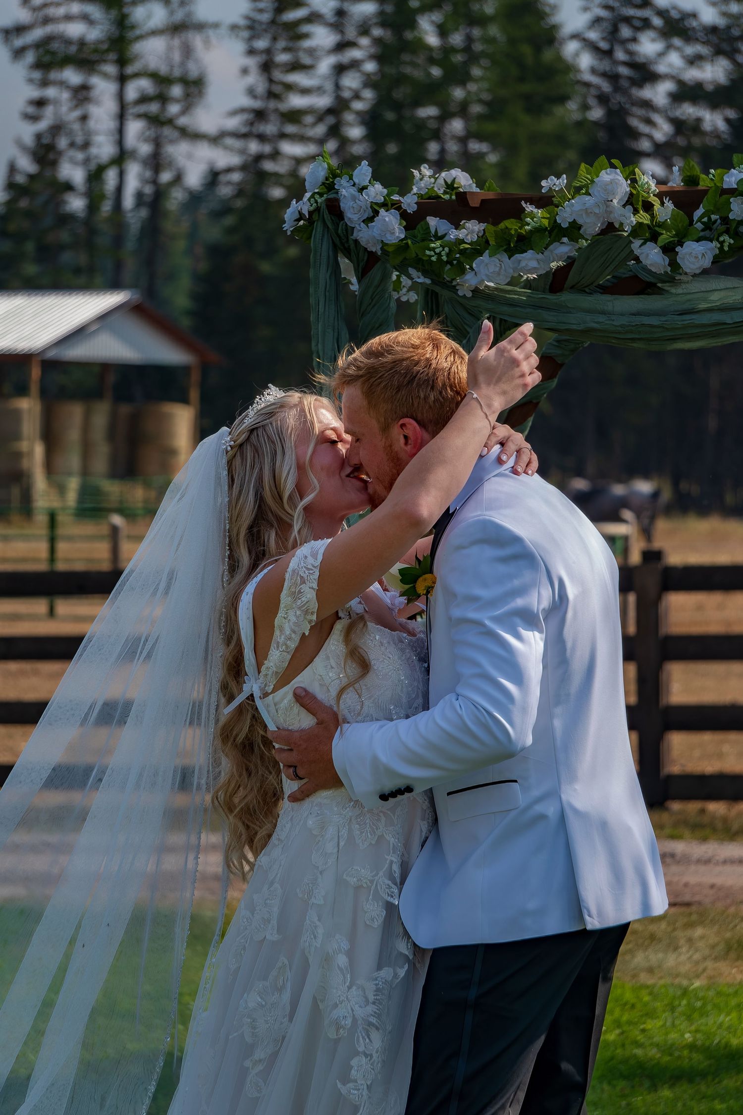 Newlyweds share their first kiss as married couple during outdoor countryside wedding.
