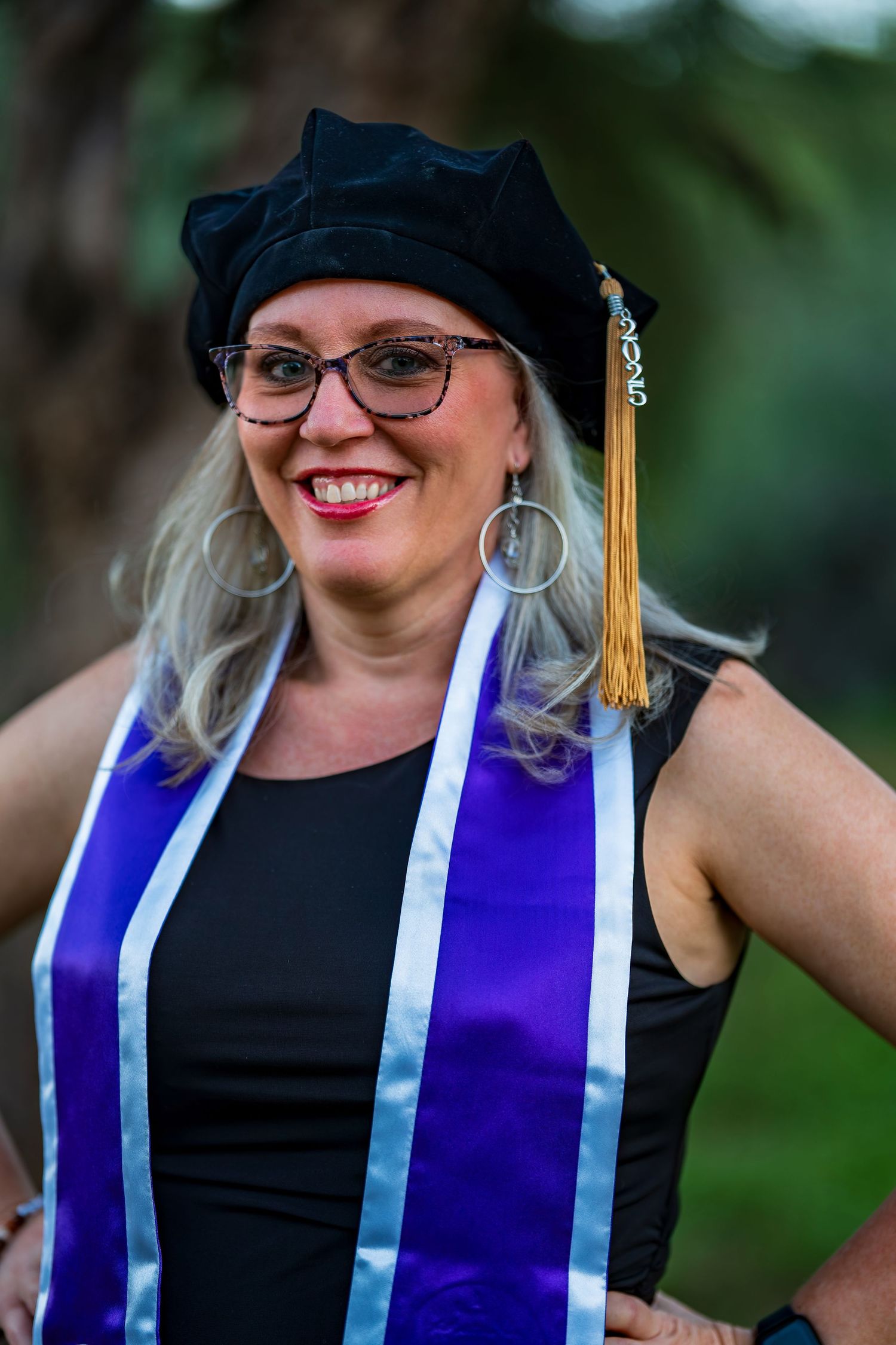 Graduate in academic regalia shows off purple stole and gold tassel while smiling.