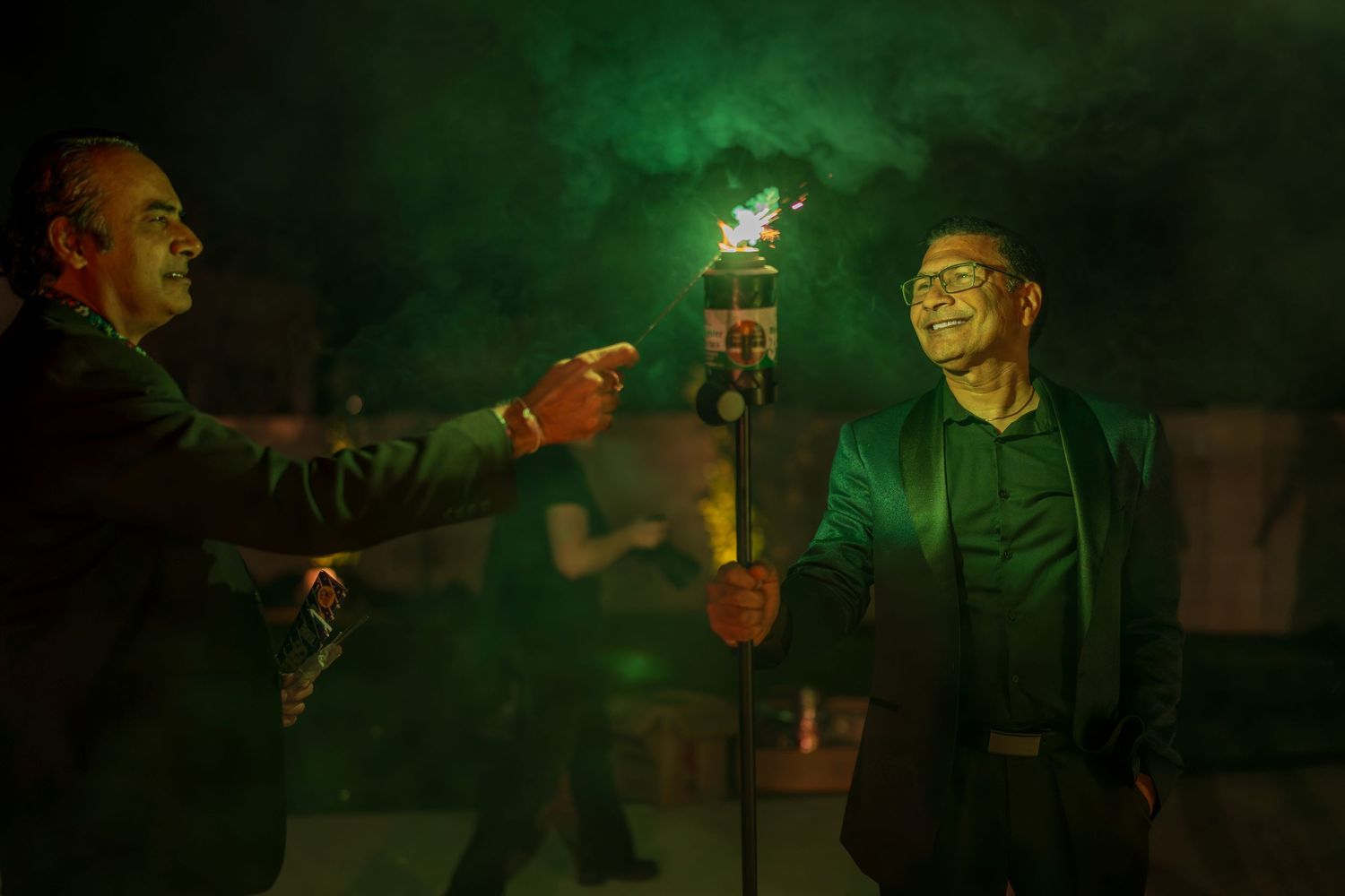 Green lighting illuminates celebrants holding sparklers during a nighttime party.
