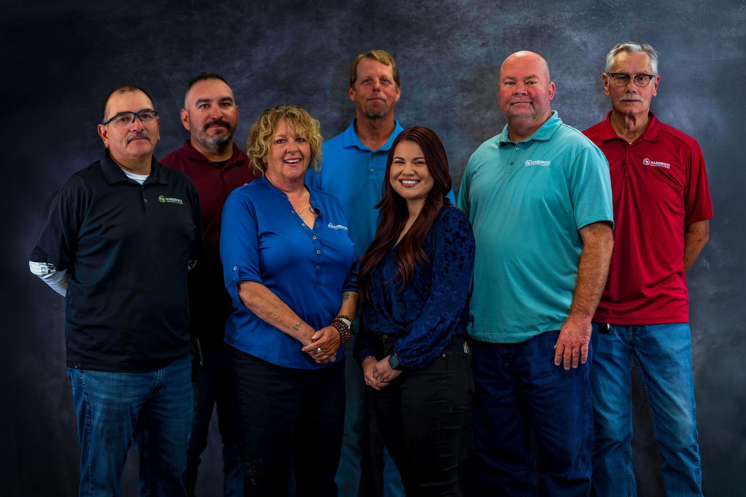 Group photo of seven employees in business casual attire against dark studio background.