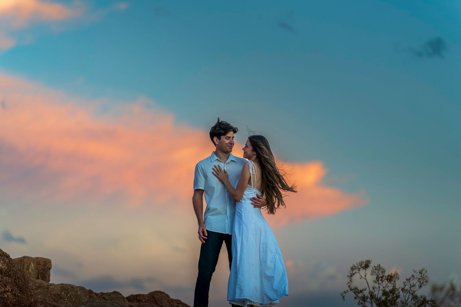 Two people share an intimate moment during golden hour with a blue and pink sky backdrop.