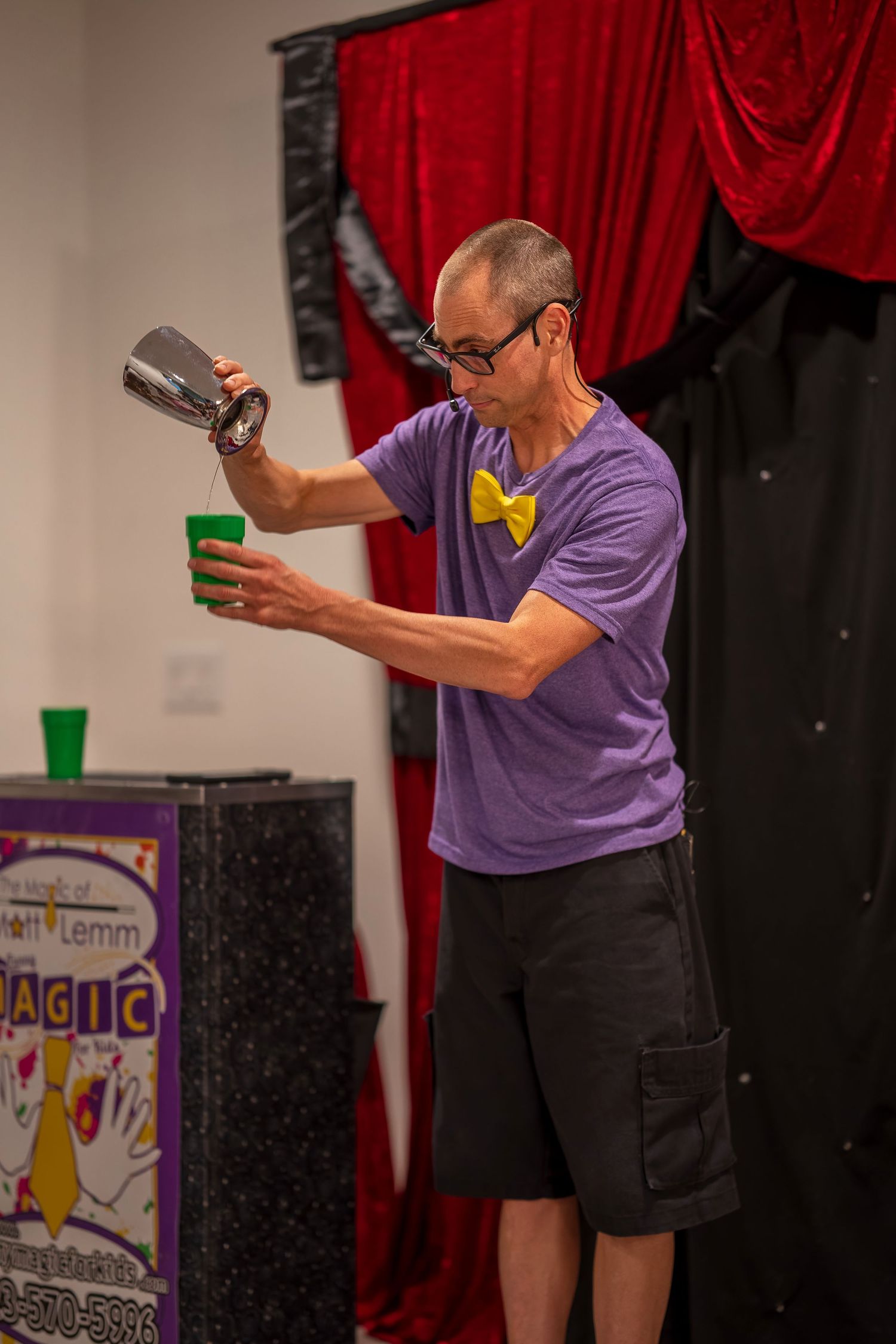 Magician pouring liquid between containers during performance with red curtain background.