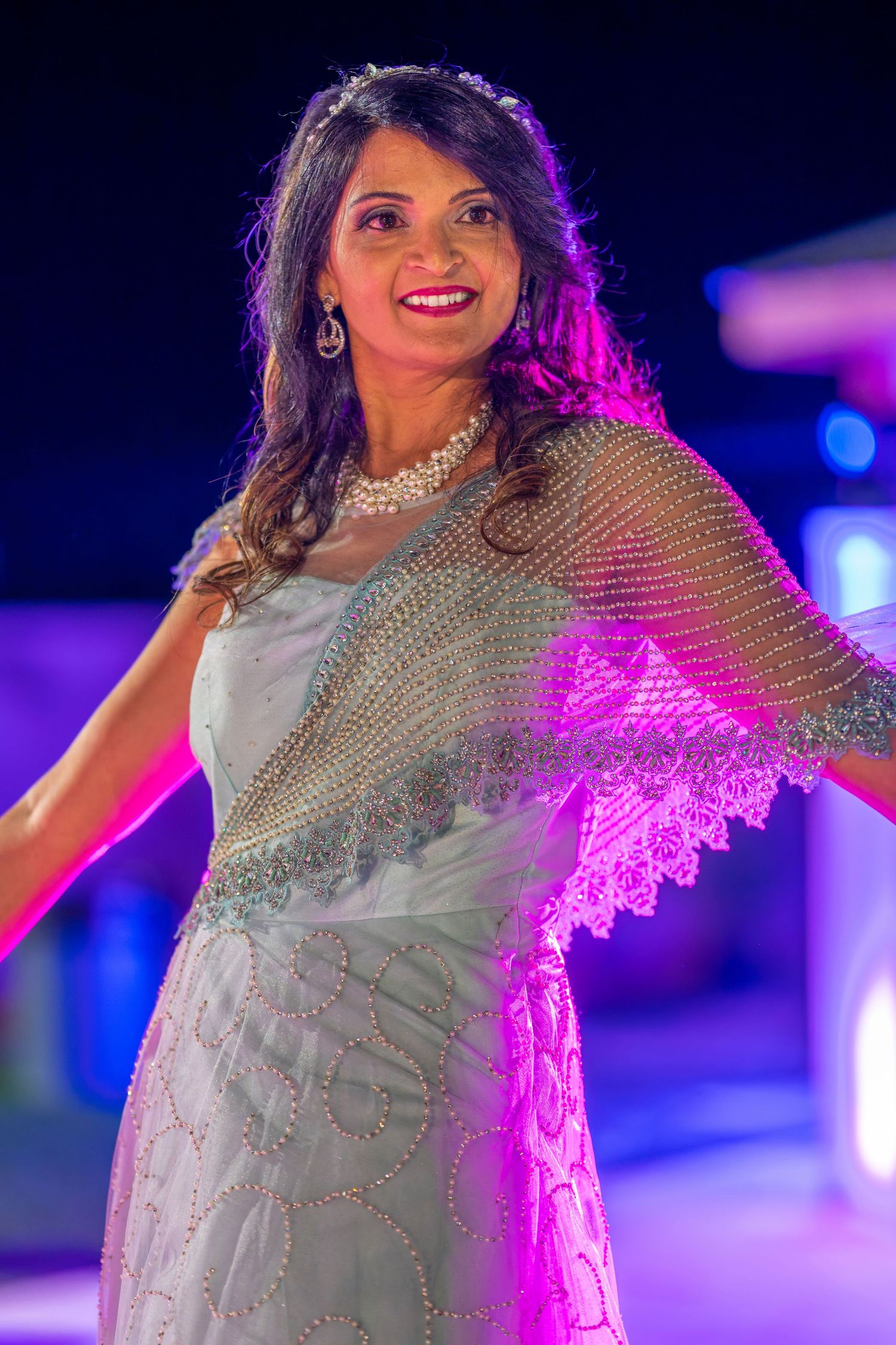Dancer in a sparkly silver dress performing under dramatic purple stage lighting.