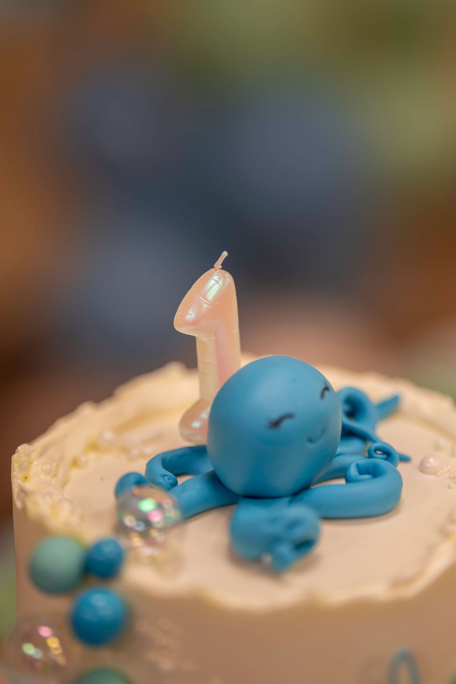 First birthday cake topped with a blue fondant octopus and number one candle with pearl decorations.
