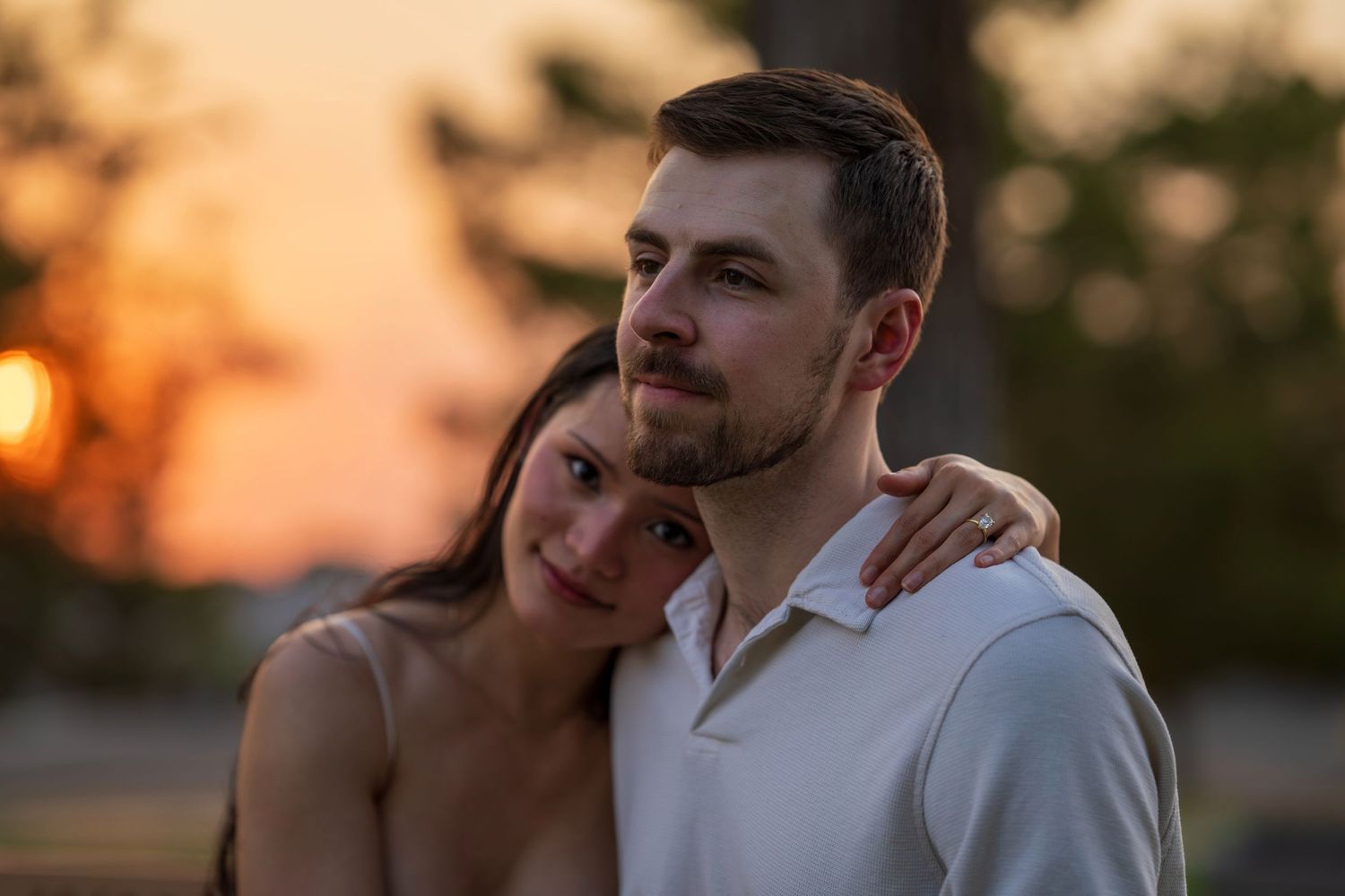 Couple embracing tenderly at sunset, man in white shirt with woman leaning on his shoulder.