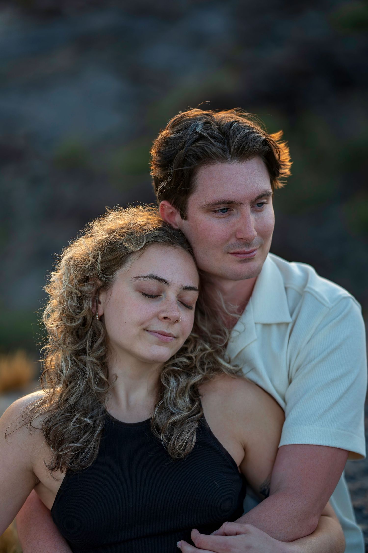 Young couple in a tender moment, woman with curly hair resting her head on mans shoulder outdoors.