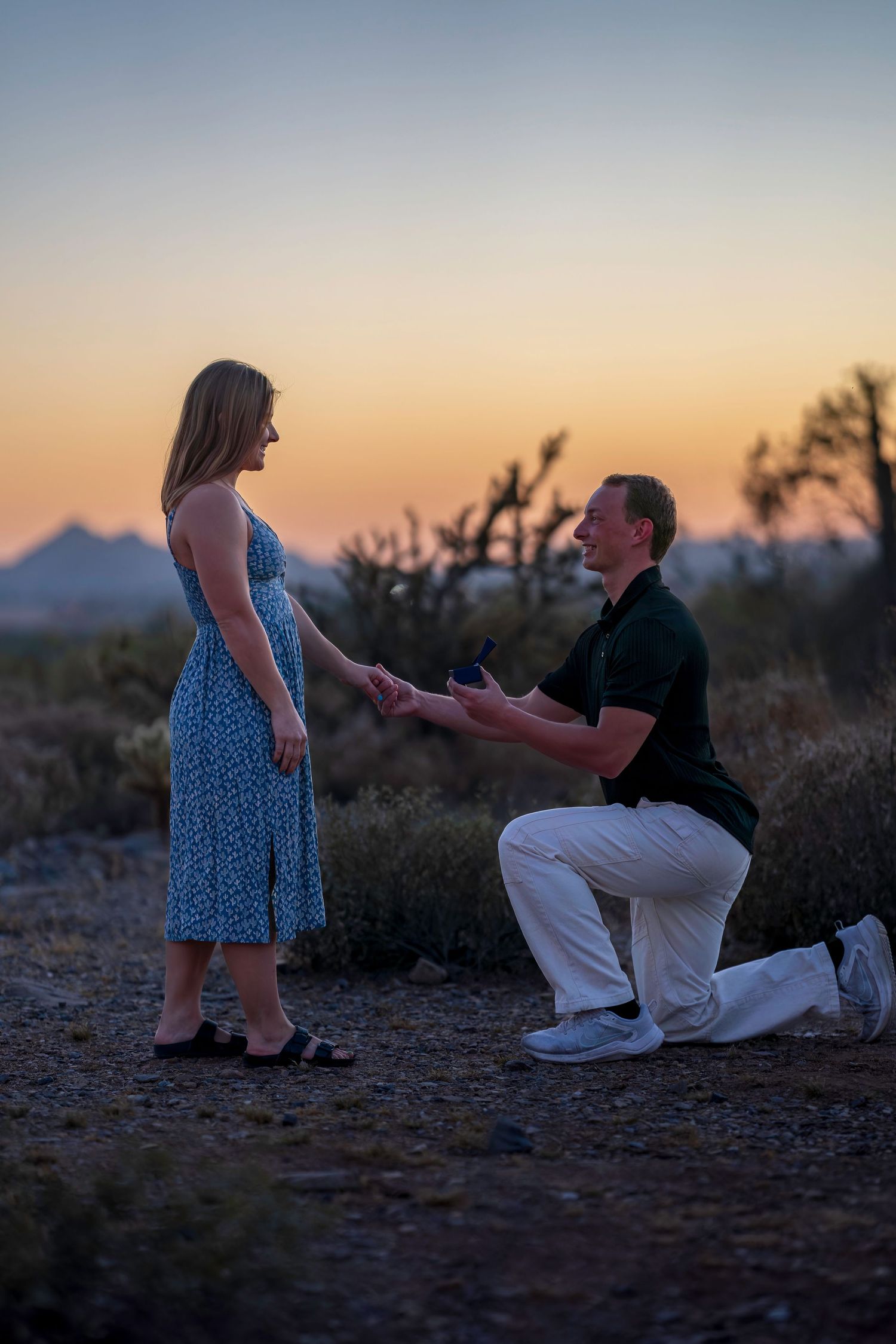 Man on one knee proposing to woman at sunset in desert landscape.