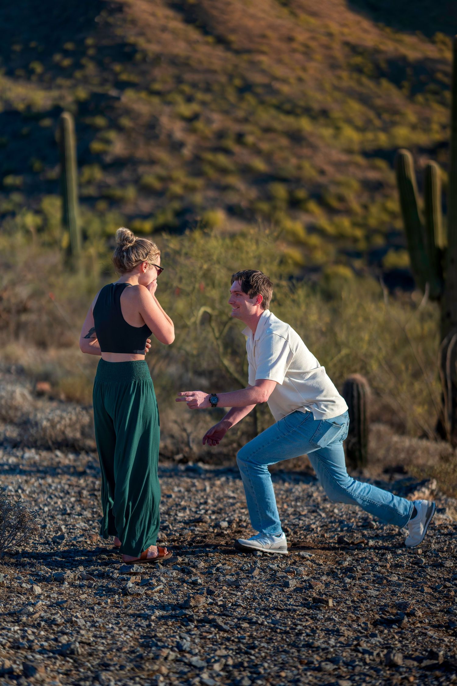 A man playfully gestures toward a woman in a desert landscape with saguaro cacti in Arizona.