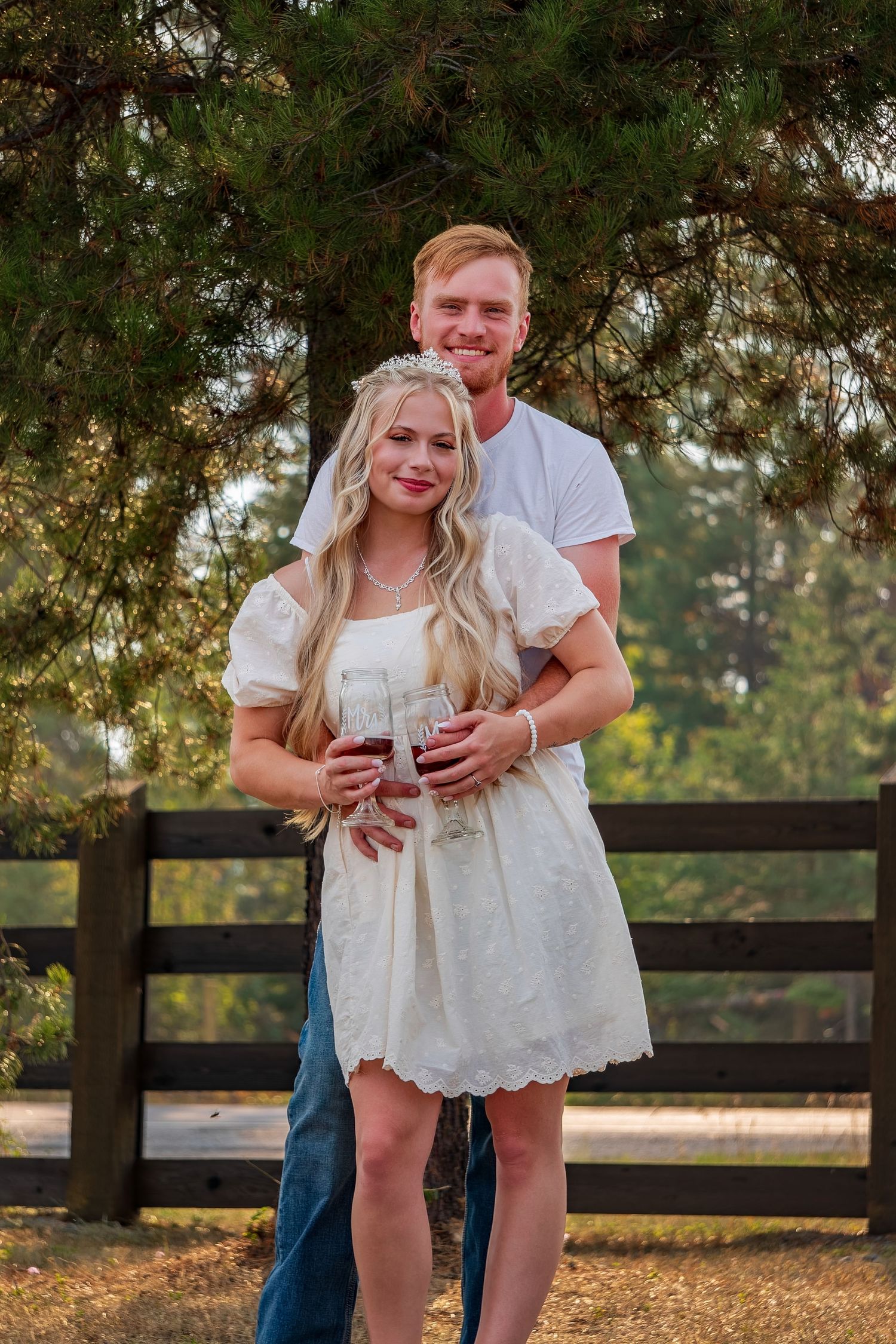 Couple posing together by wooden fence during golden hour.