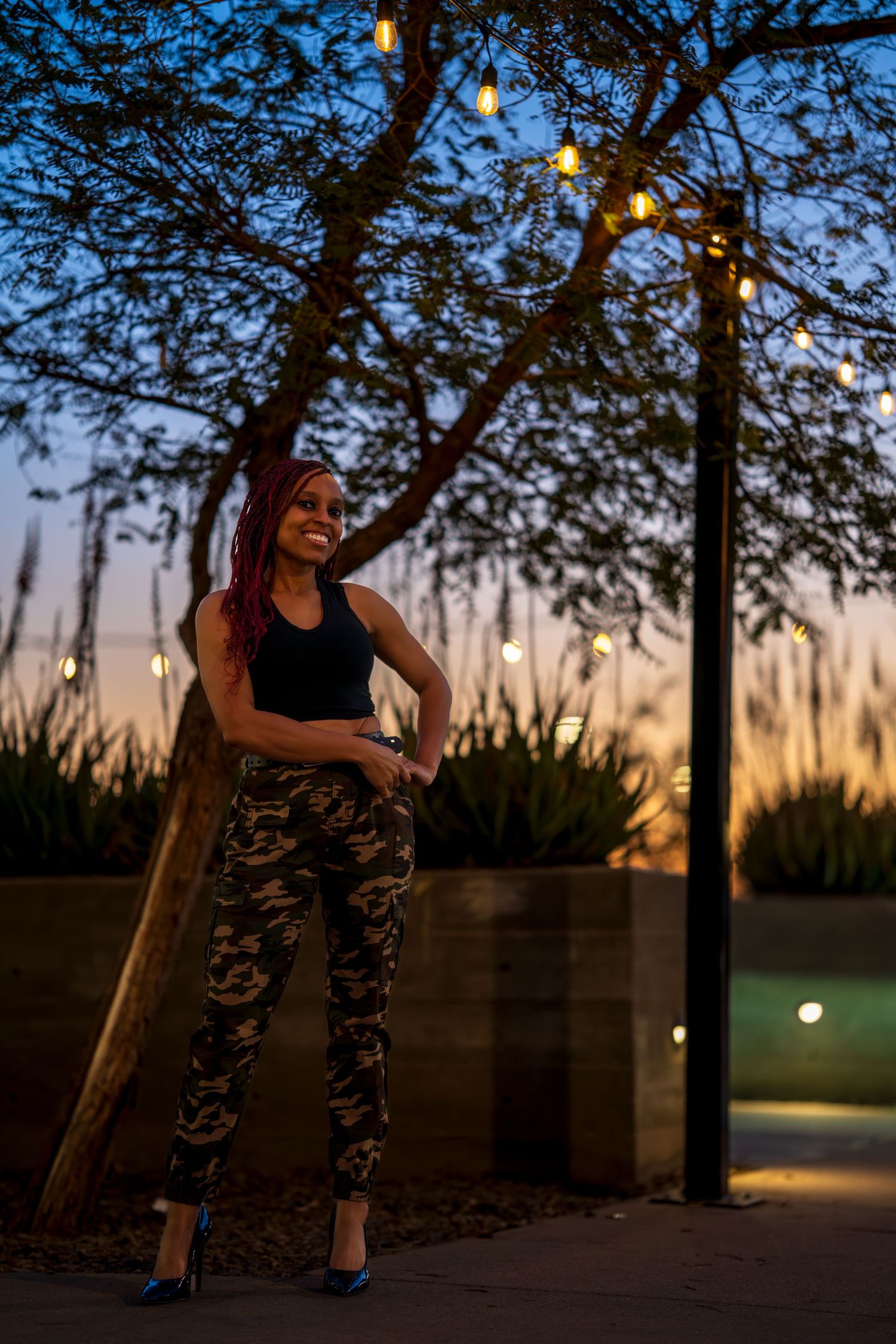 Stylish outdoor portrait with tree silhouettes and string lights at twilight.