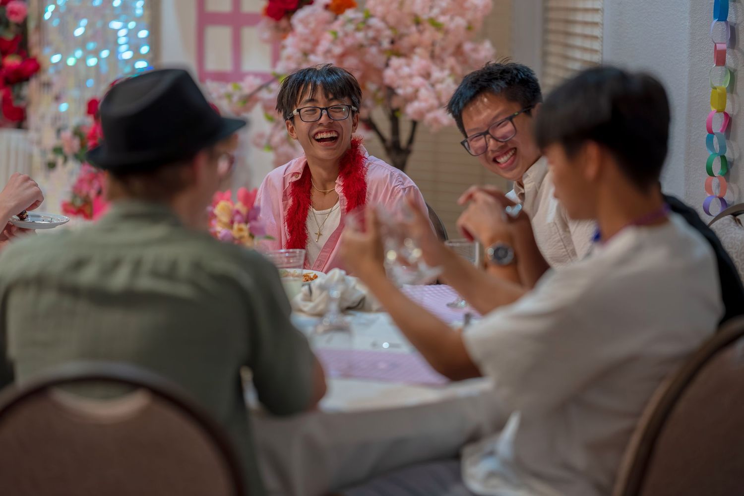 Guests seated at tables during a celebration with pink and floral decorations visible in the background.