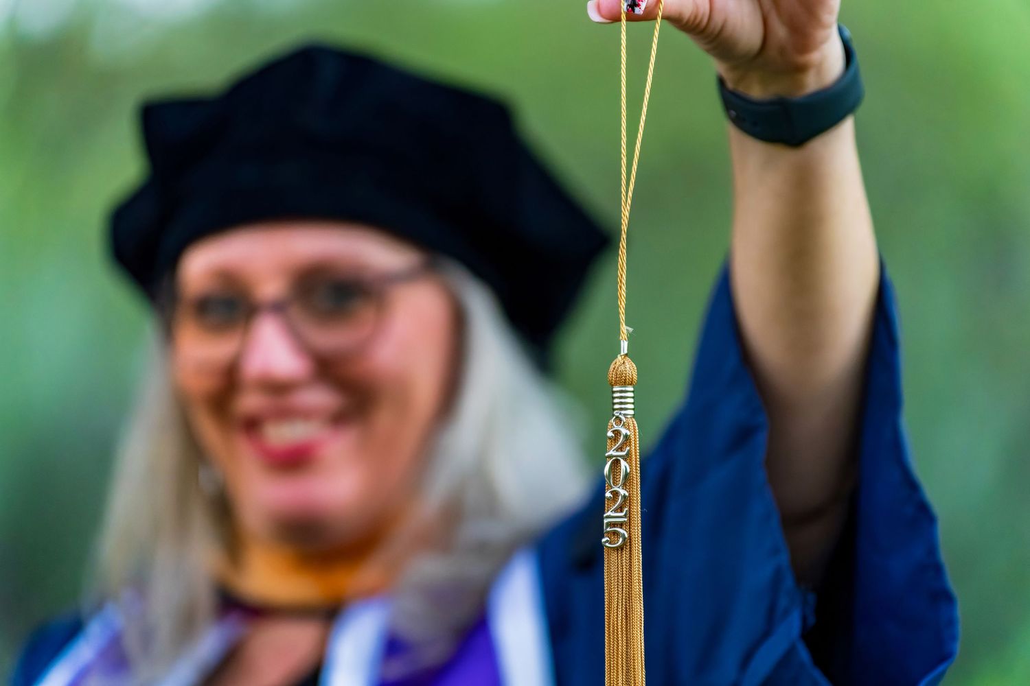 Graduate in academic dress holds tassel while celebrating outdoors.