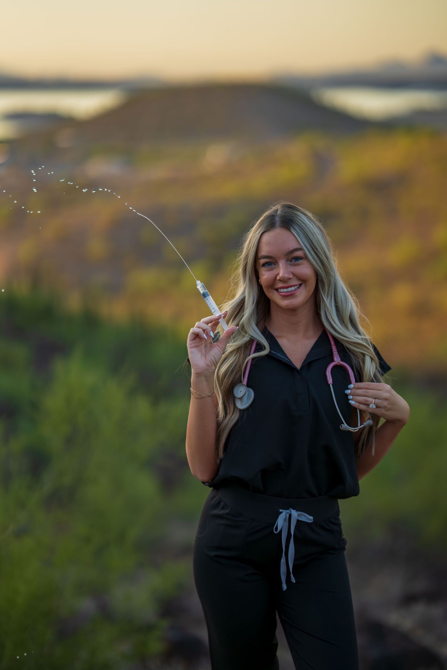 Healthcare professional in black scrubs poses playfully against desert landscape with saguaro cacti at sunset.