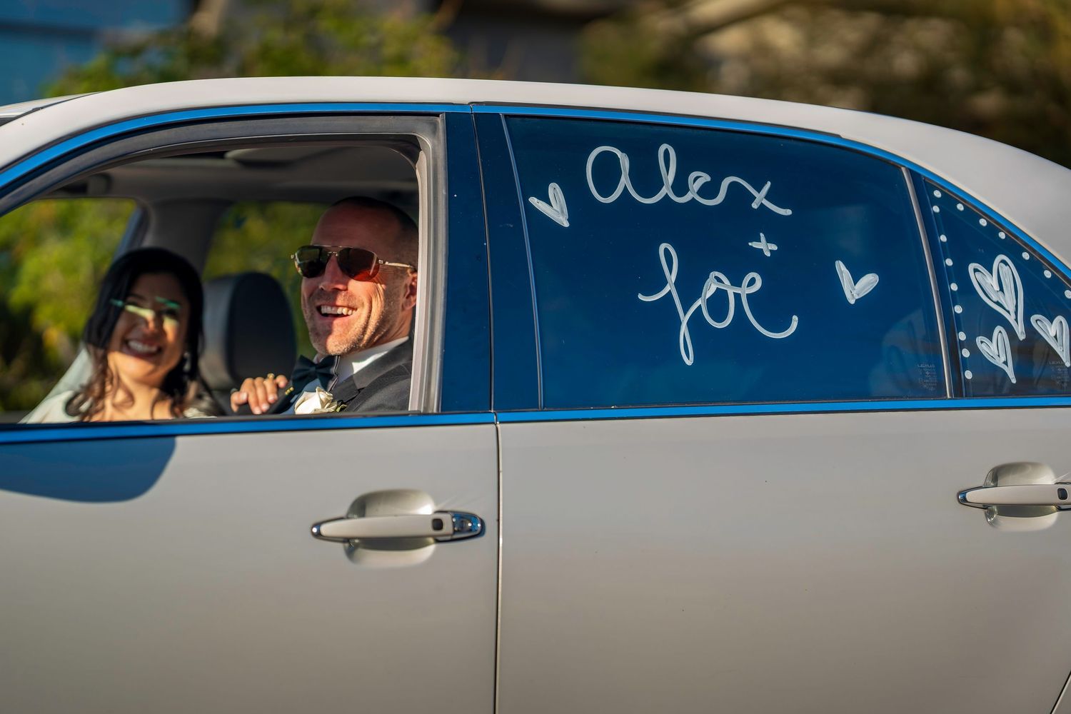 Newlyweds Alex and Joe smile inside decorated getaway car after wedding ceremony.