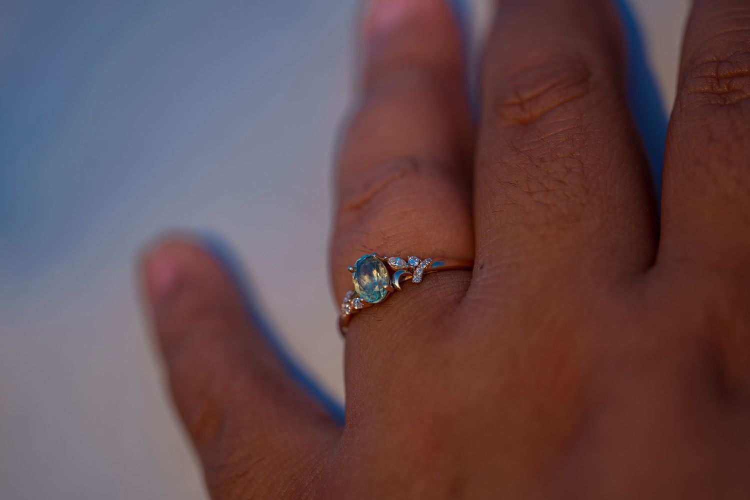 Close-up of a hand wearing a delicate gold ring with a blue gemstone and small diamond accents.