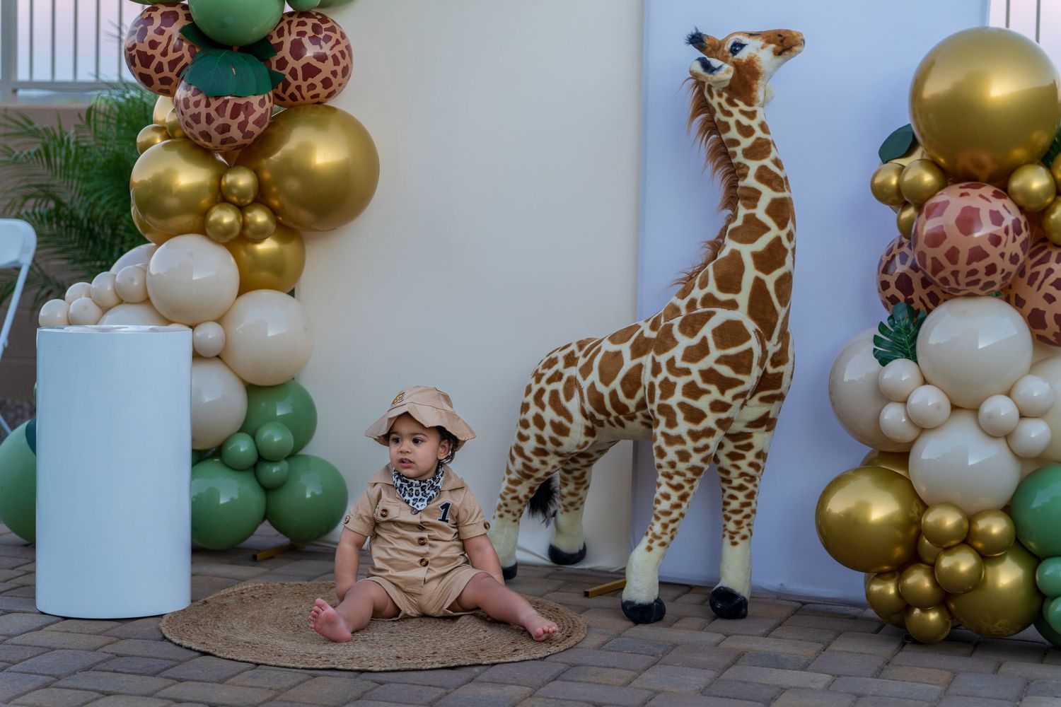 Safari-themed party setup with balloon garlands, a large giraffe decoration, and tropical greenery.
