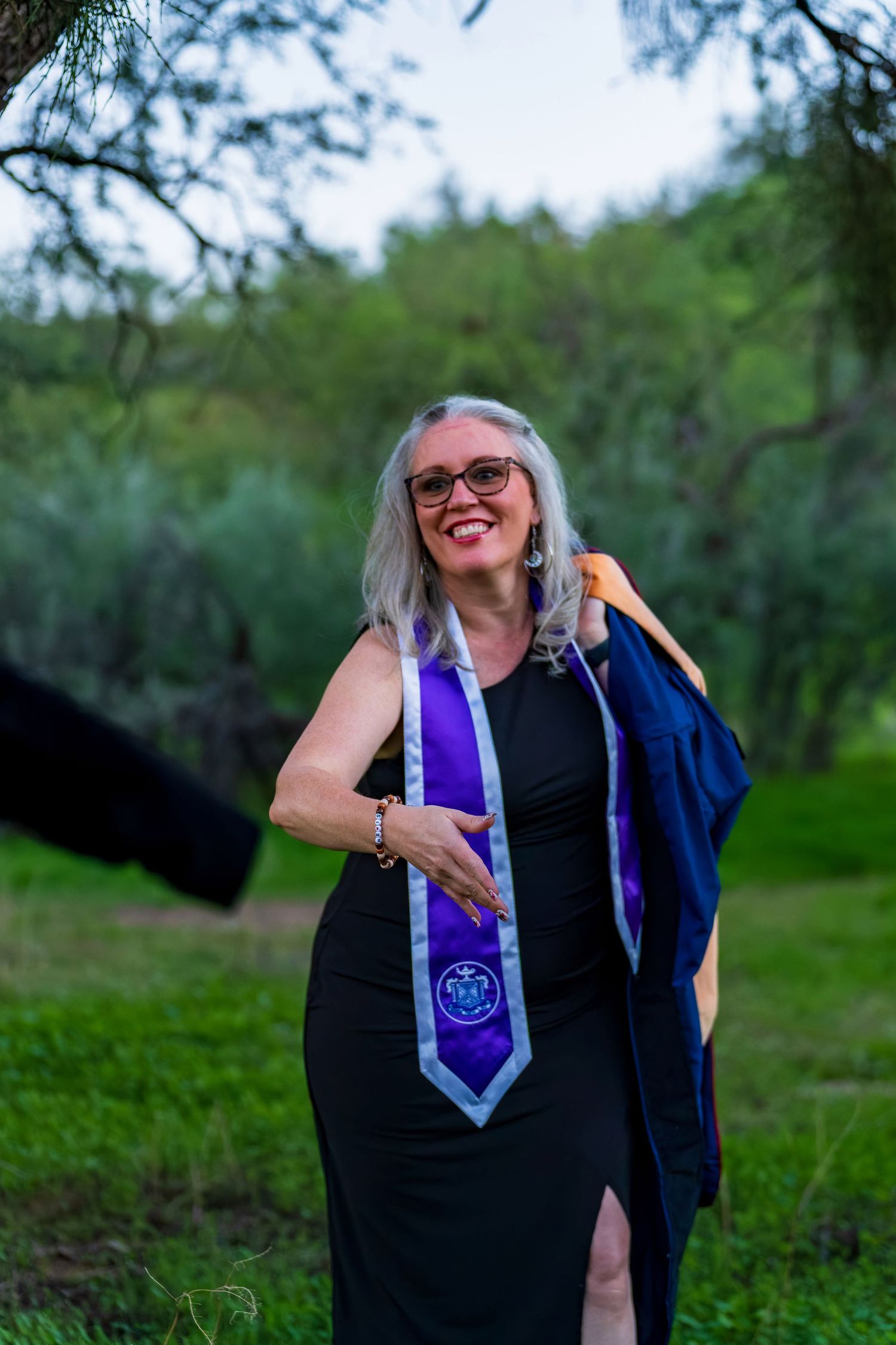 Graduate in academic regalia posing outdoors with purple stole.