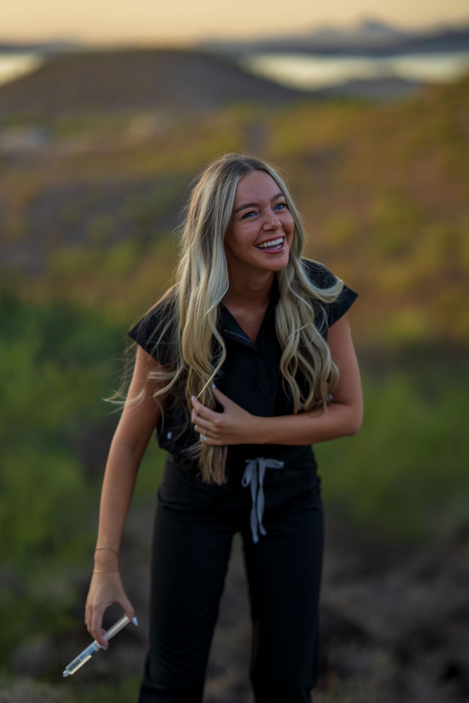 Healthcare worker in black uniform laughs during outdoor desert photoshoot at sunset.