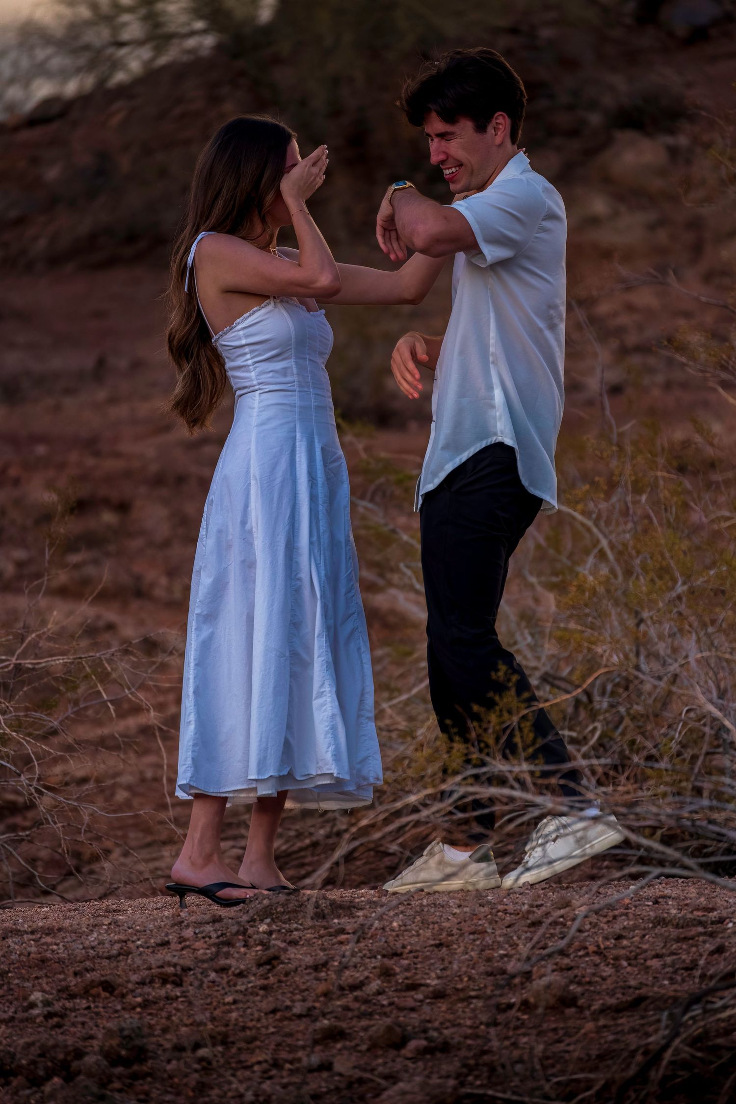 Playful couple in white dress and casual attire share a joyful moment outdoors.