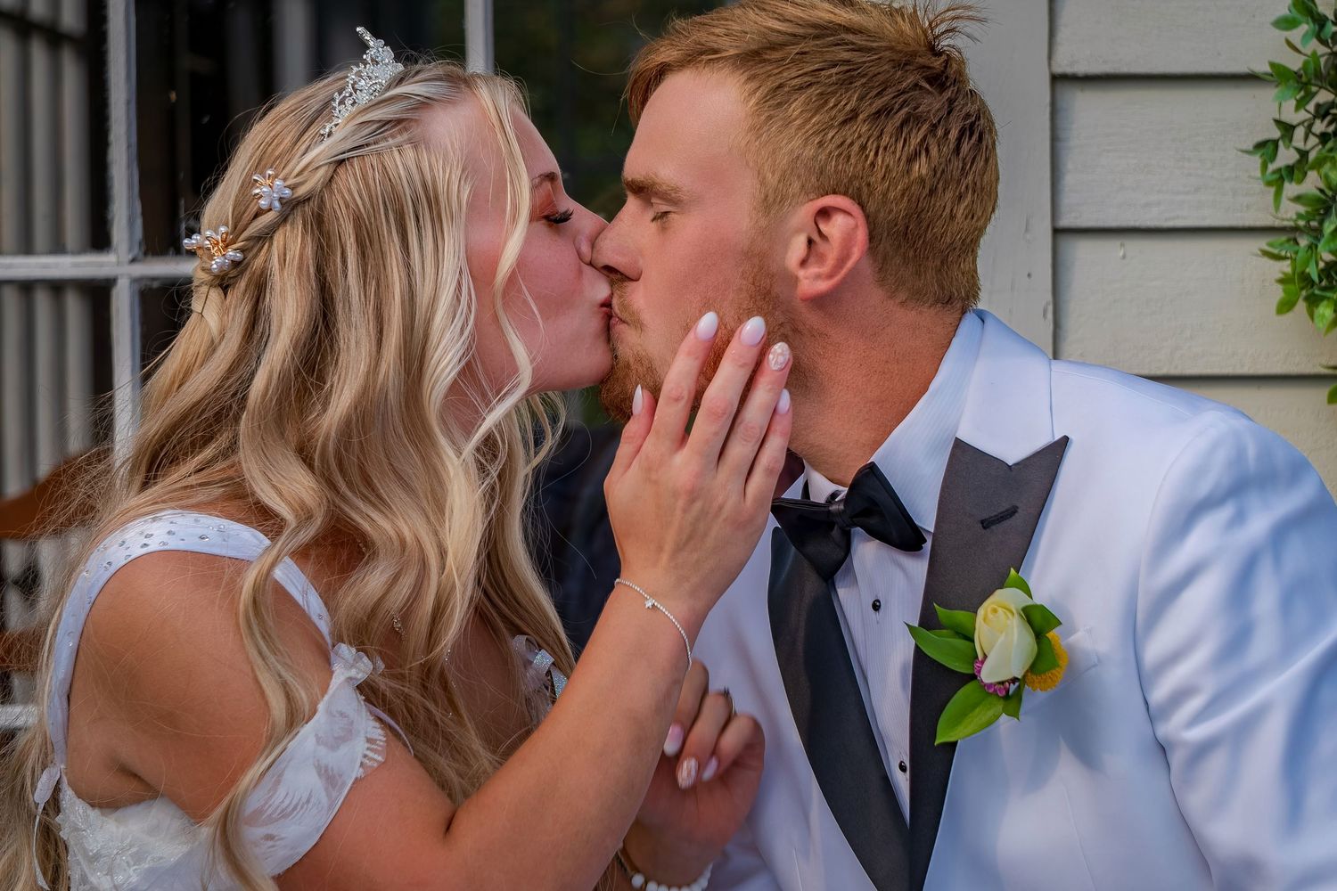 Romantic wedding kiss between couple in formal attire outdoors.