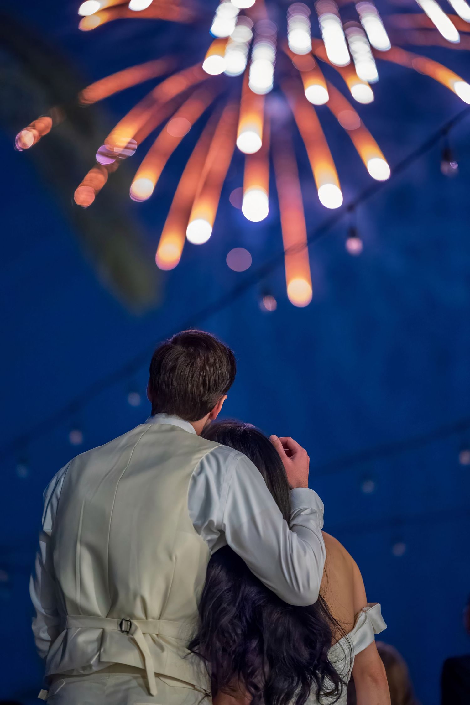 Romantic moment under bursting fireworks display at nighttime wedding celebration.