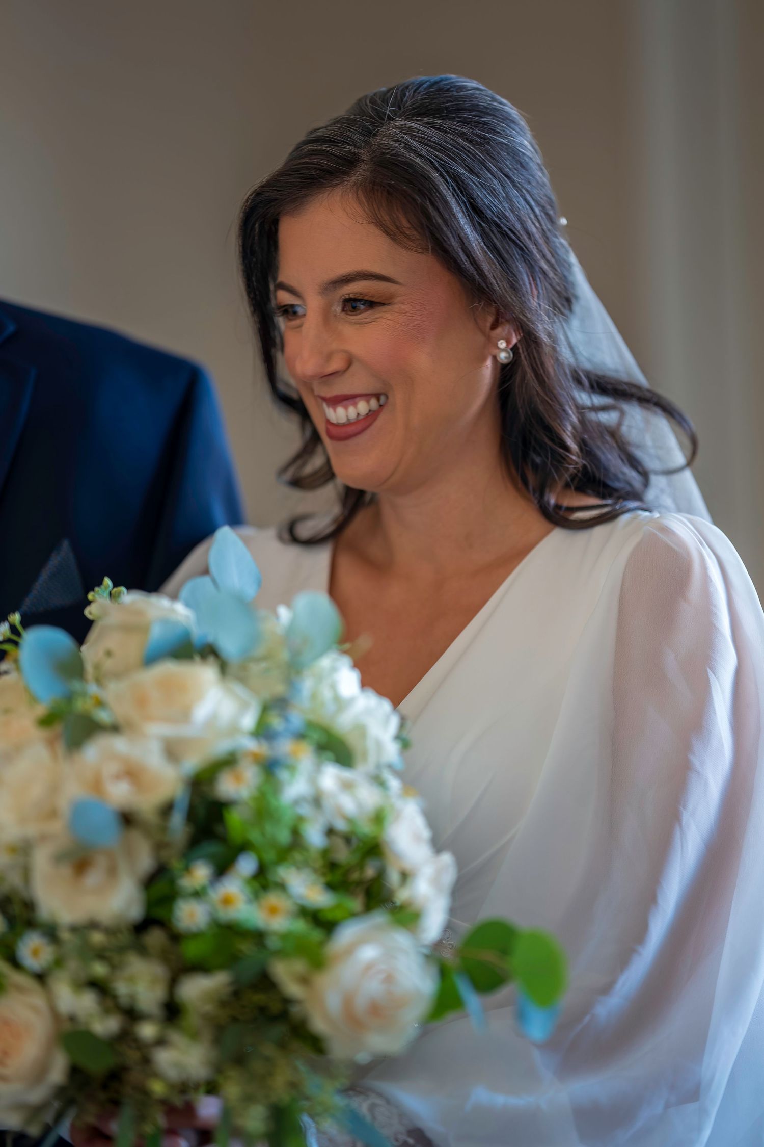 Radiant bride laughing while holding white and blue floral bouquet on her wedding day.