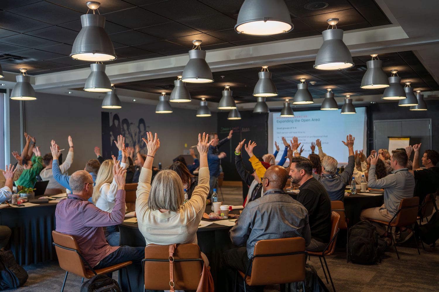 Conference attendees participate in a presentation in a modern meeting space with industrial lighting.