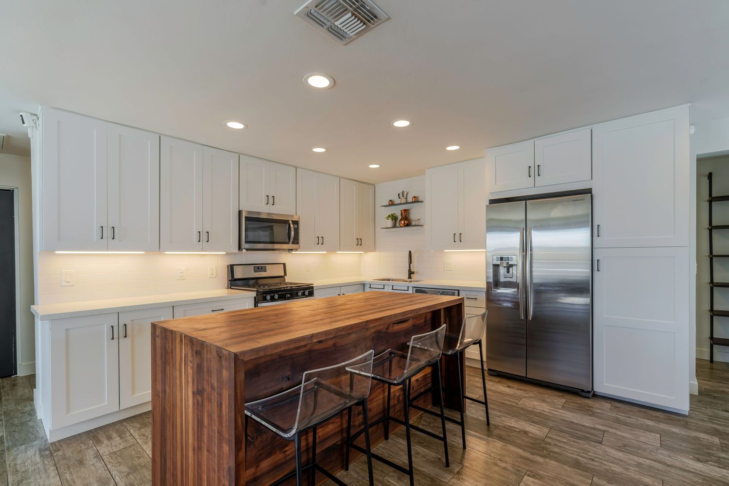 Modern kitchen with white cabinets, butcher block island, bar stools, stainless steel appliances, and hardwood floors.