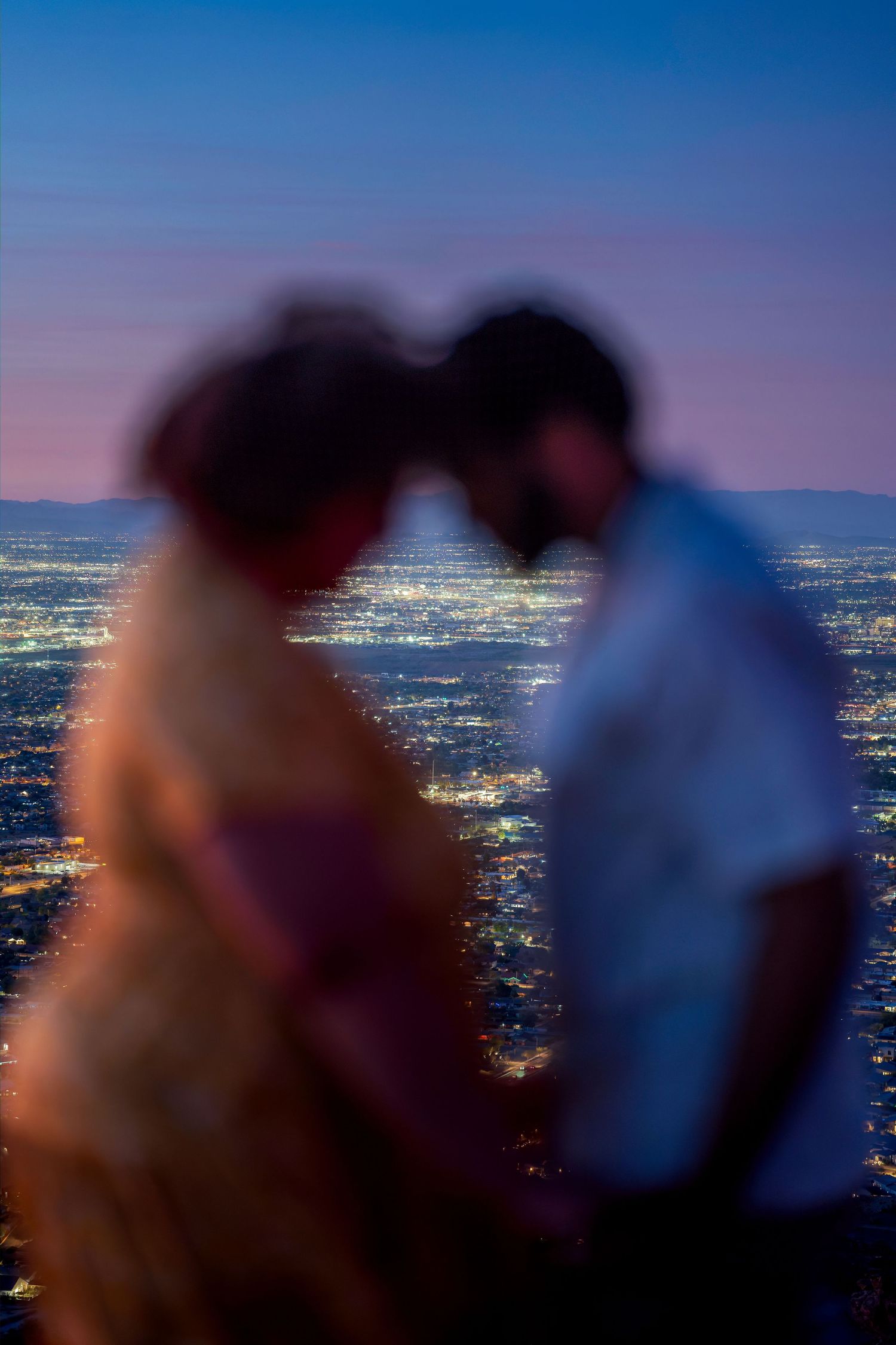 Blurred romantic couple touching foreheads against glittering city lights at dusk.
