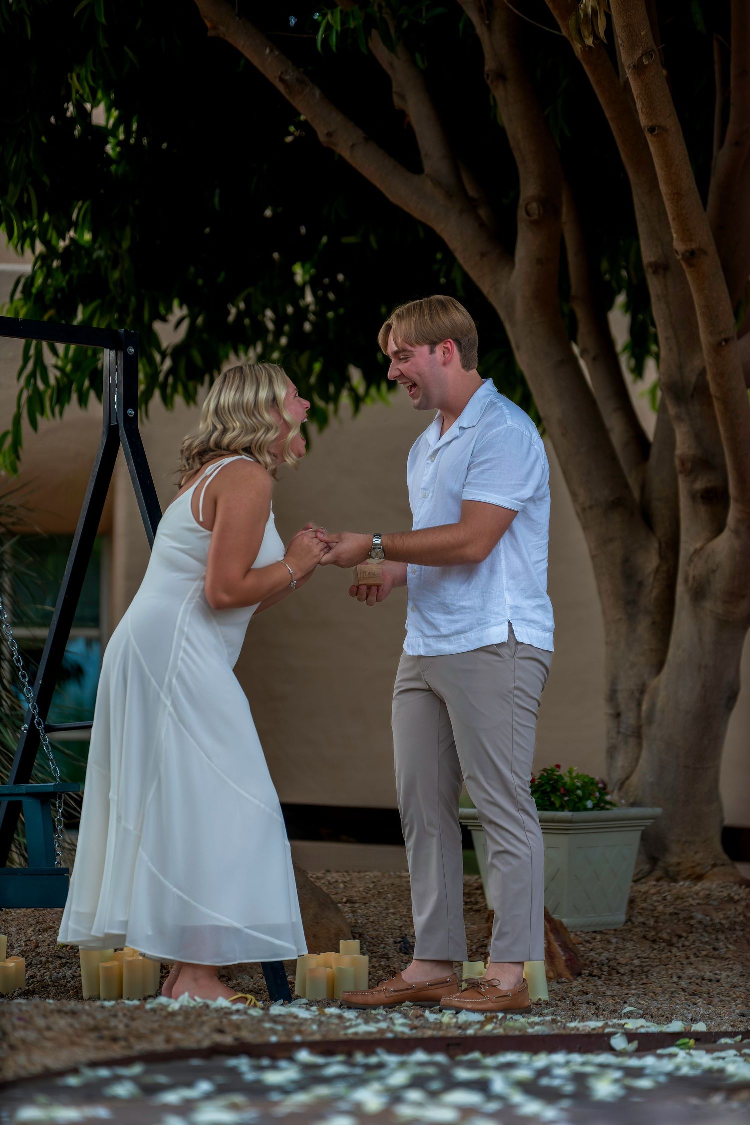 Couple sharing a joyful engagement moment surrounded by candles outdoors.