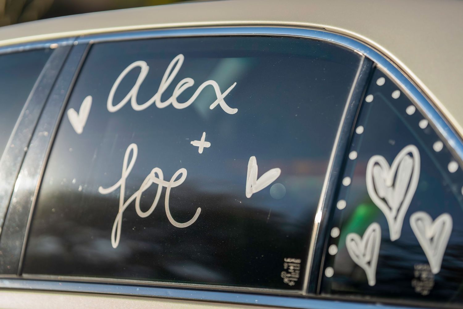 Car window decorated with Alex and Joe written in white with hearts for wedding celebration.