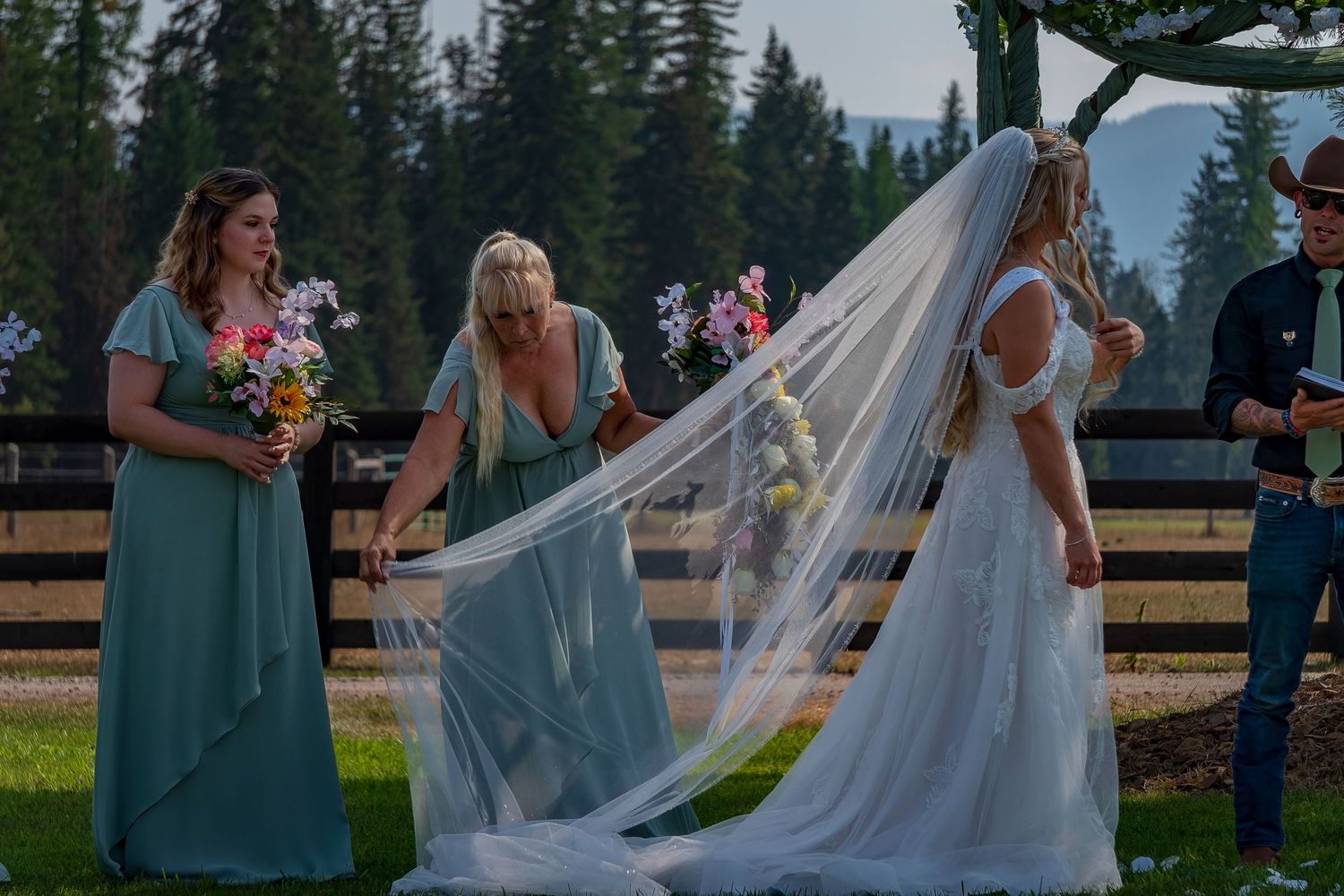 Wedding guests gather on a lawn with mountains and evergreen trees creating a scenic backdrop.