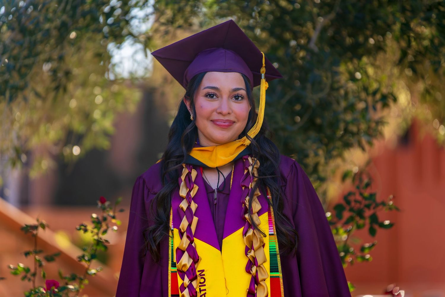 Graduate wearing academic regalia with kente cloth stole outdoors during graduation photoshoot.
