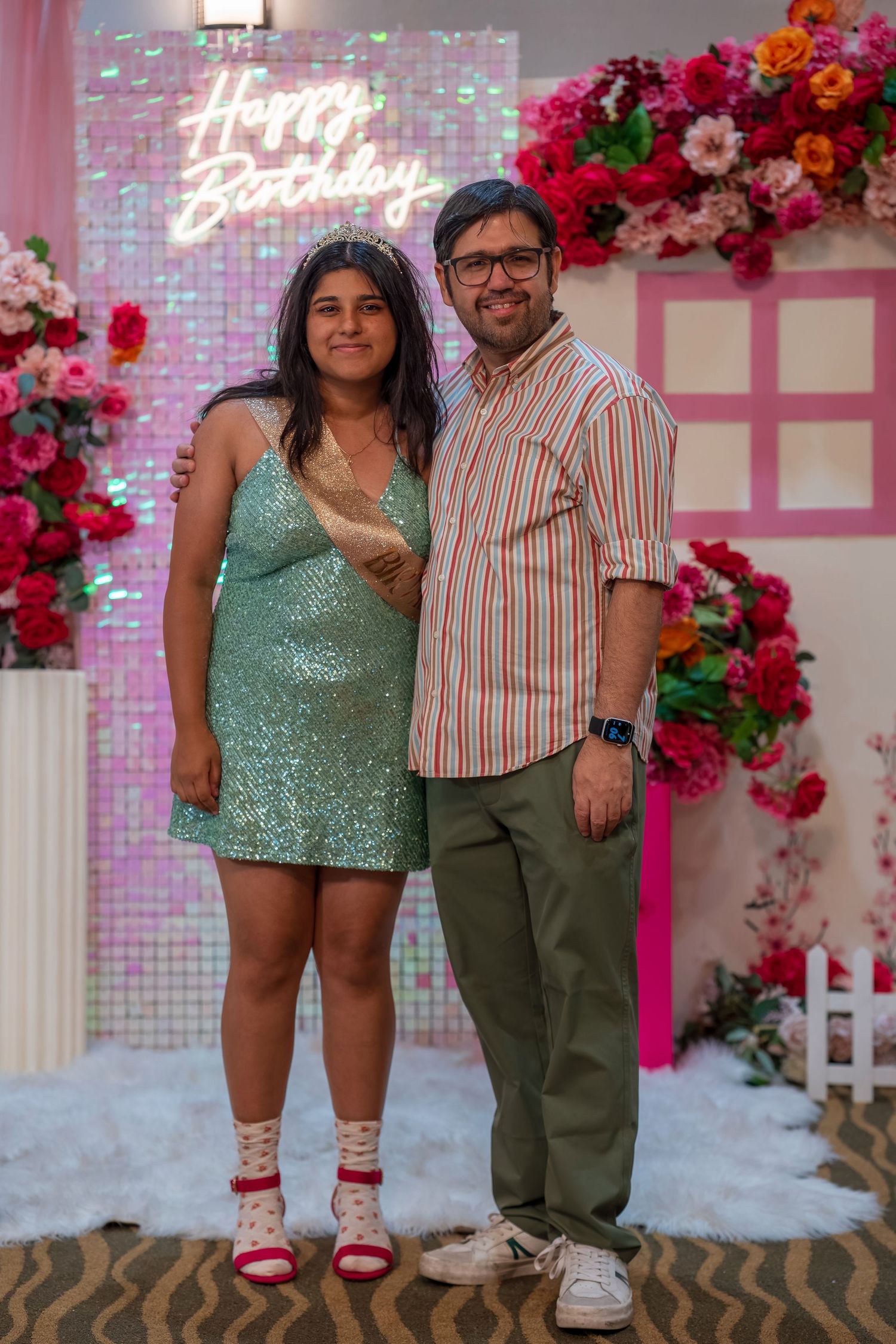 A celebration photo against a pink floral backdrop with decorative elements and lighting.