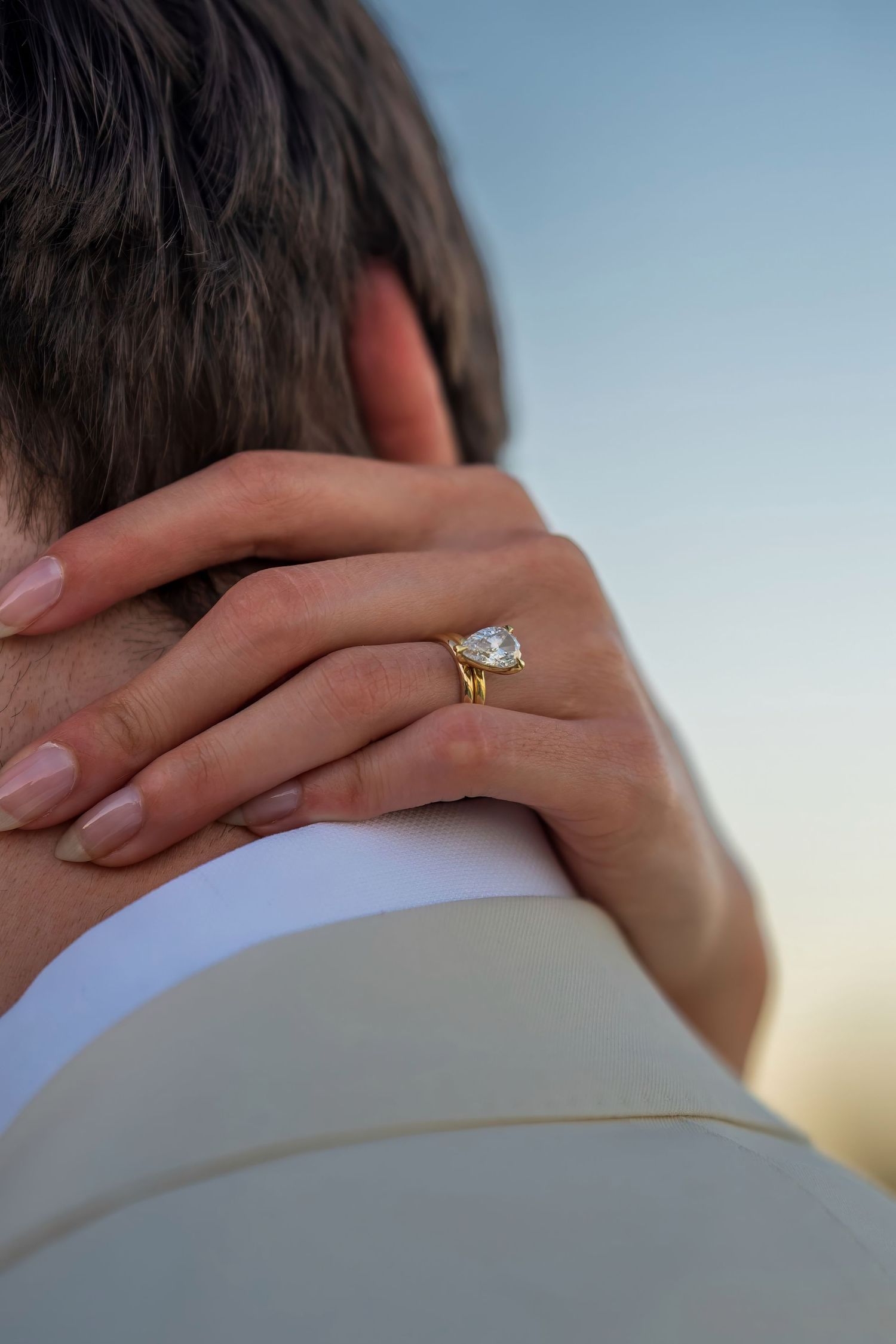 Close-up of a diamond engagement ring as hands embrace during a romantic moment.