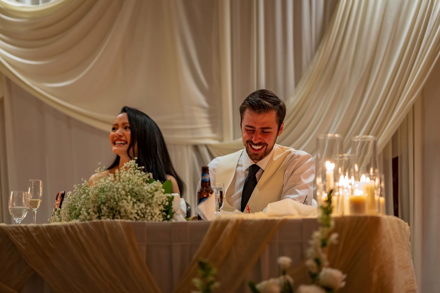 Wedding reception venue features elegant white draping and warm lighting creating a romantic atmosphere.