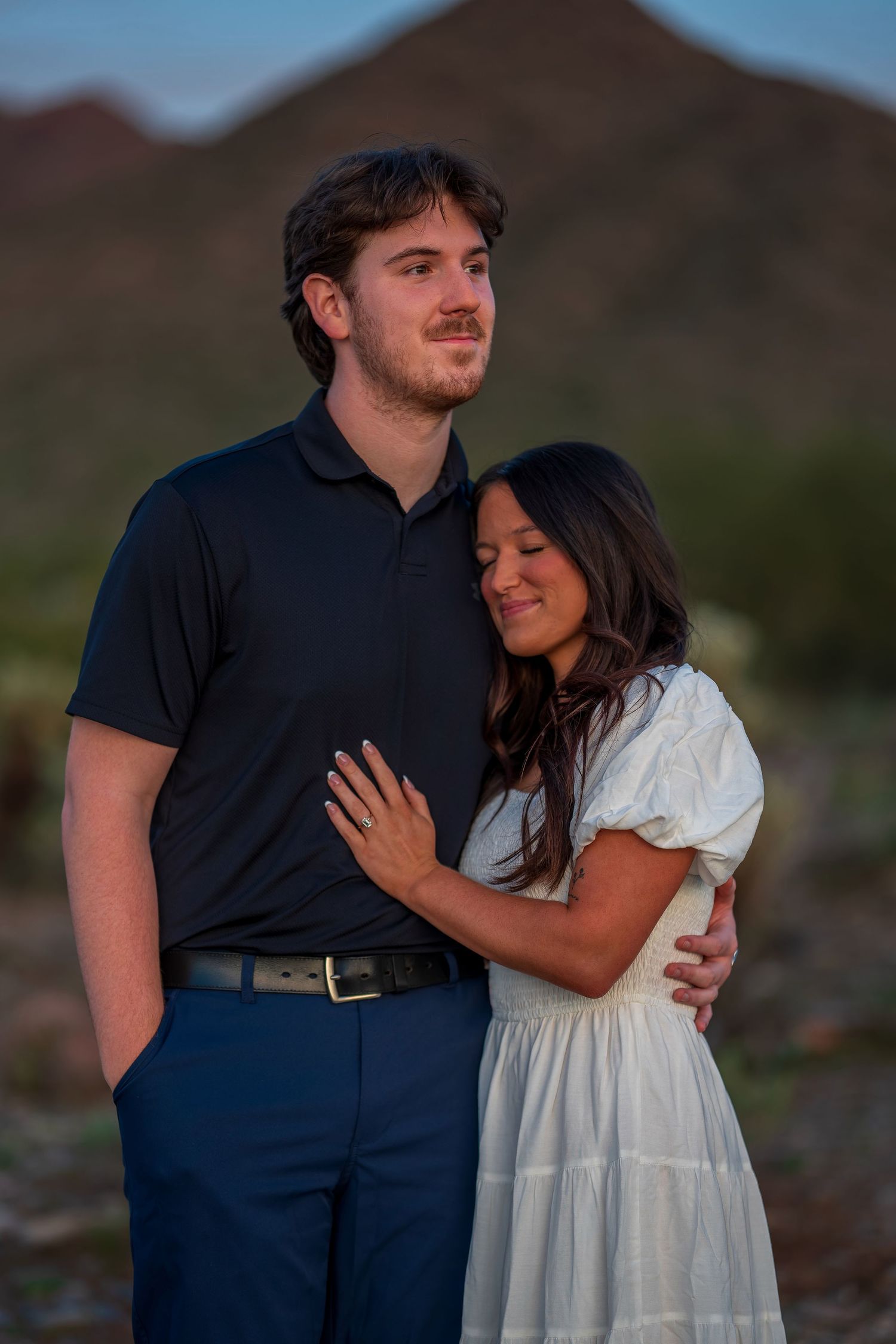 Couple in coordinated outfits pose lovingly together against a desert mountain backdrop.