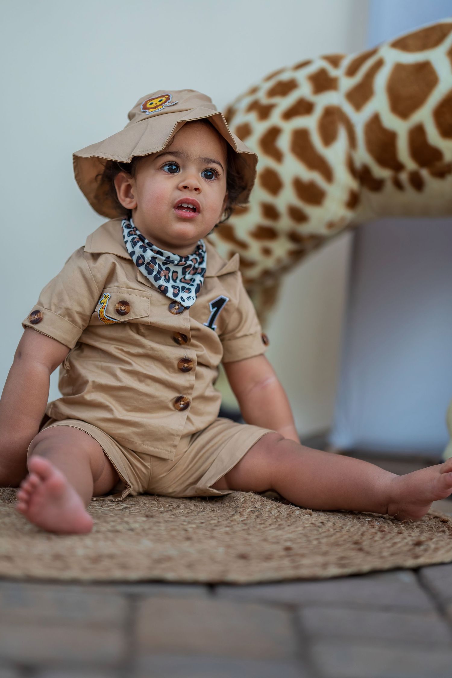 Safari-themed birthday outfit with tan explorer costume and hat next to decorative giraffe.