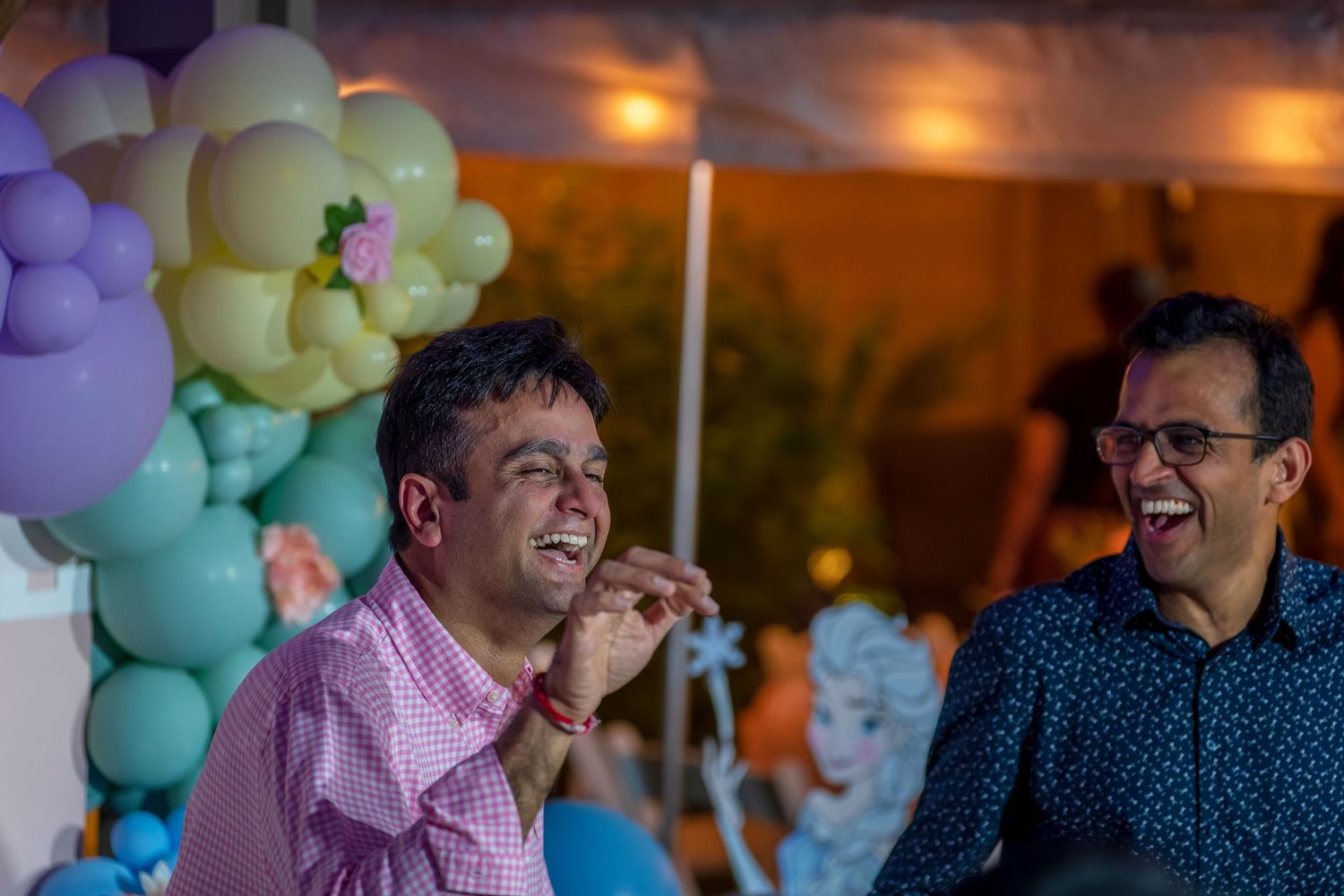 Partygoers celebrating under ambient lighting with pastel balloon decorations in the background.