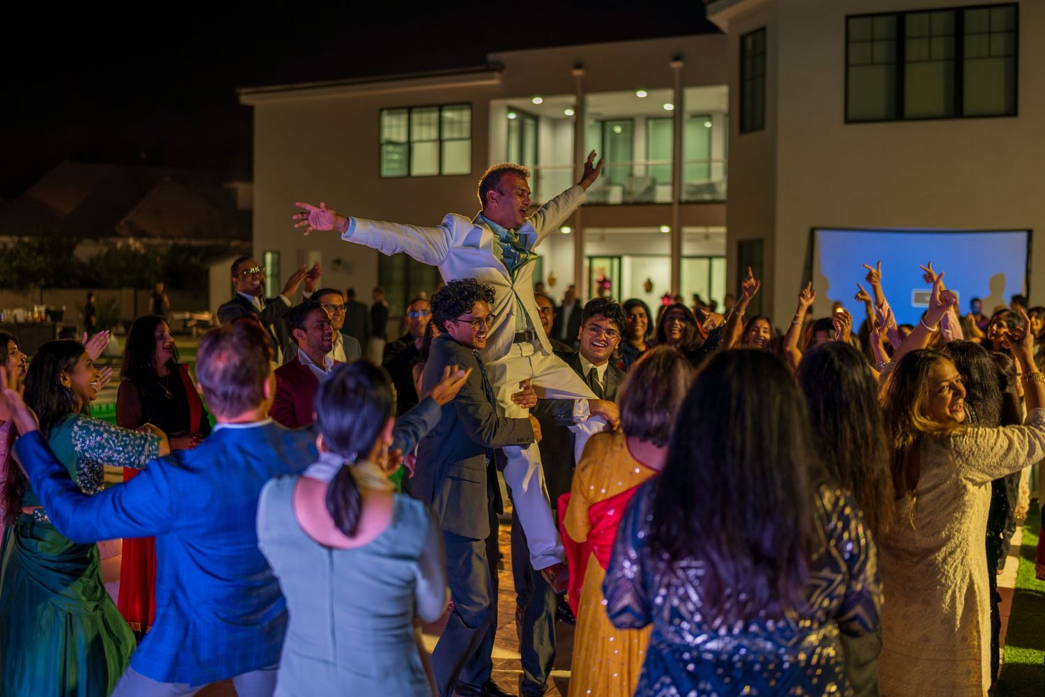 A large crowd gathers outside a building for an evening celebration with colored lights.