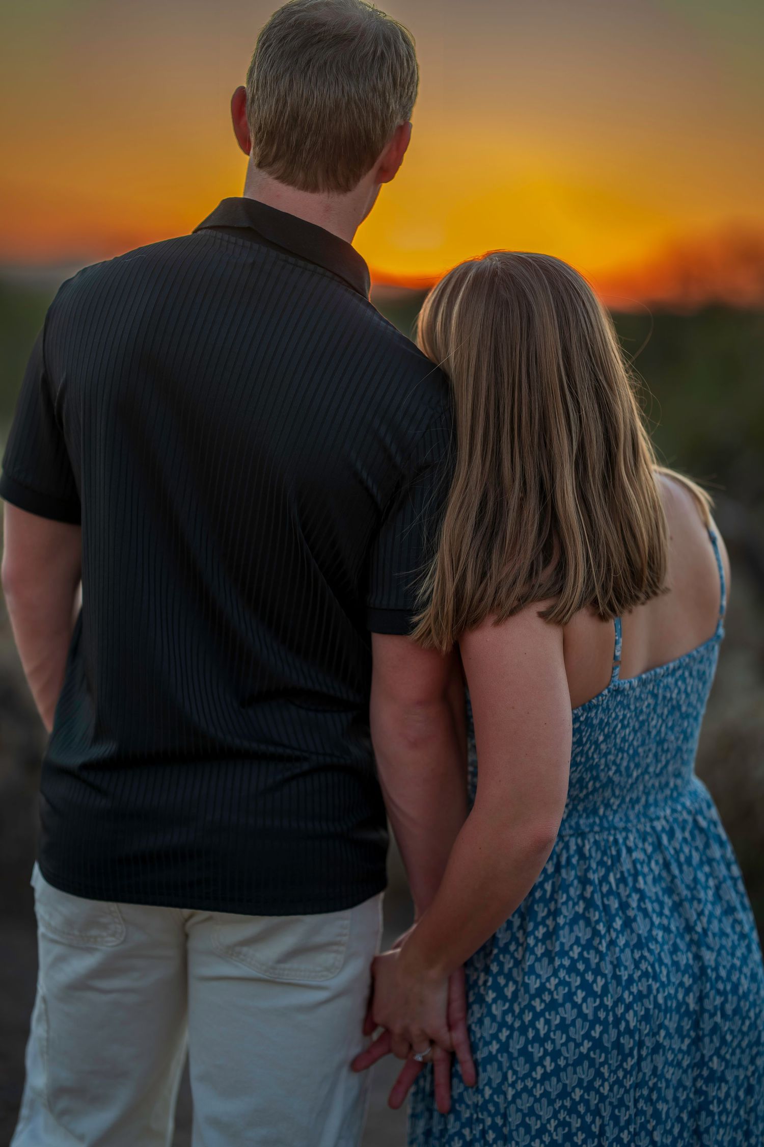 Couple holding hands watching vibrant orange sunset together in desert setting.