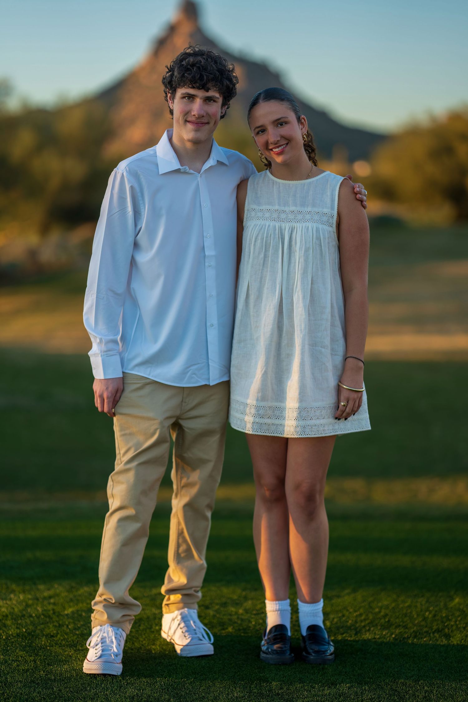 Children in white outfits standing together on grass during sunset photoshoot.