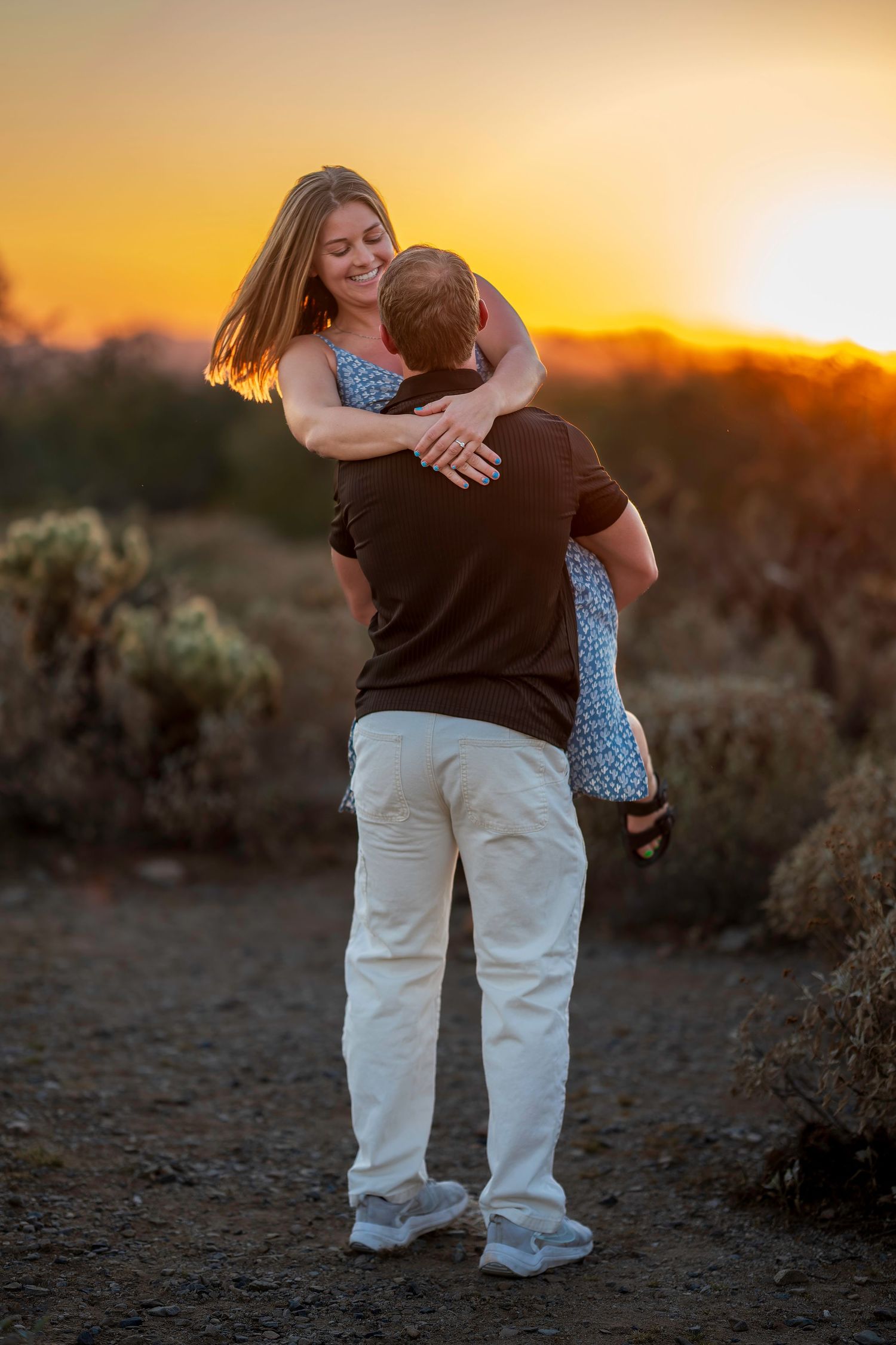 Couple embracing at sunset in a desert landscape, woman smiling as man lifts her during golden hour.
