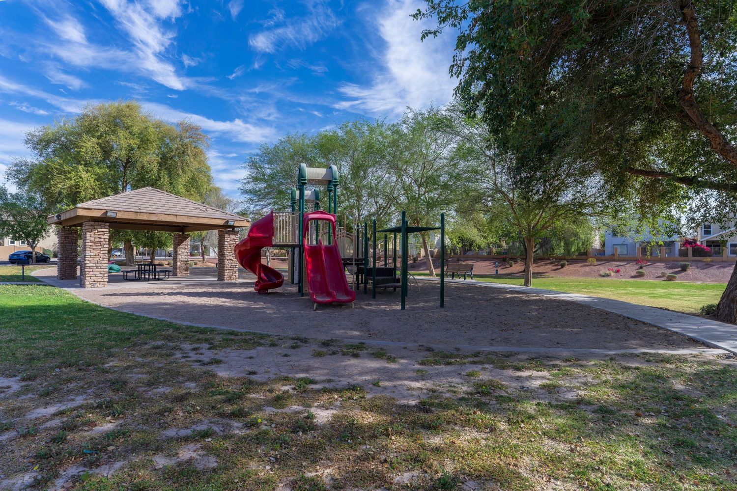 Community park with red playground equipment, gazebo, green grass, and mature shade trees.