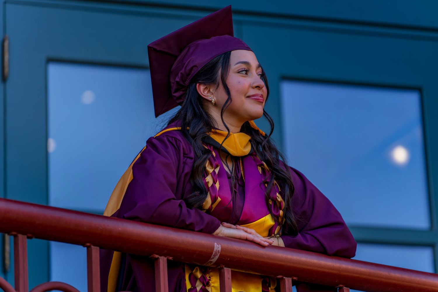 Graduate in academic dress poses against evening sky during graduation photo session.