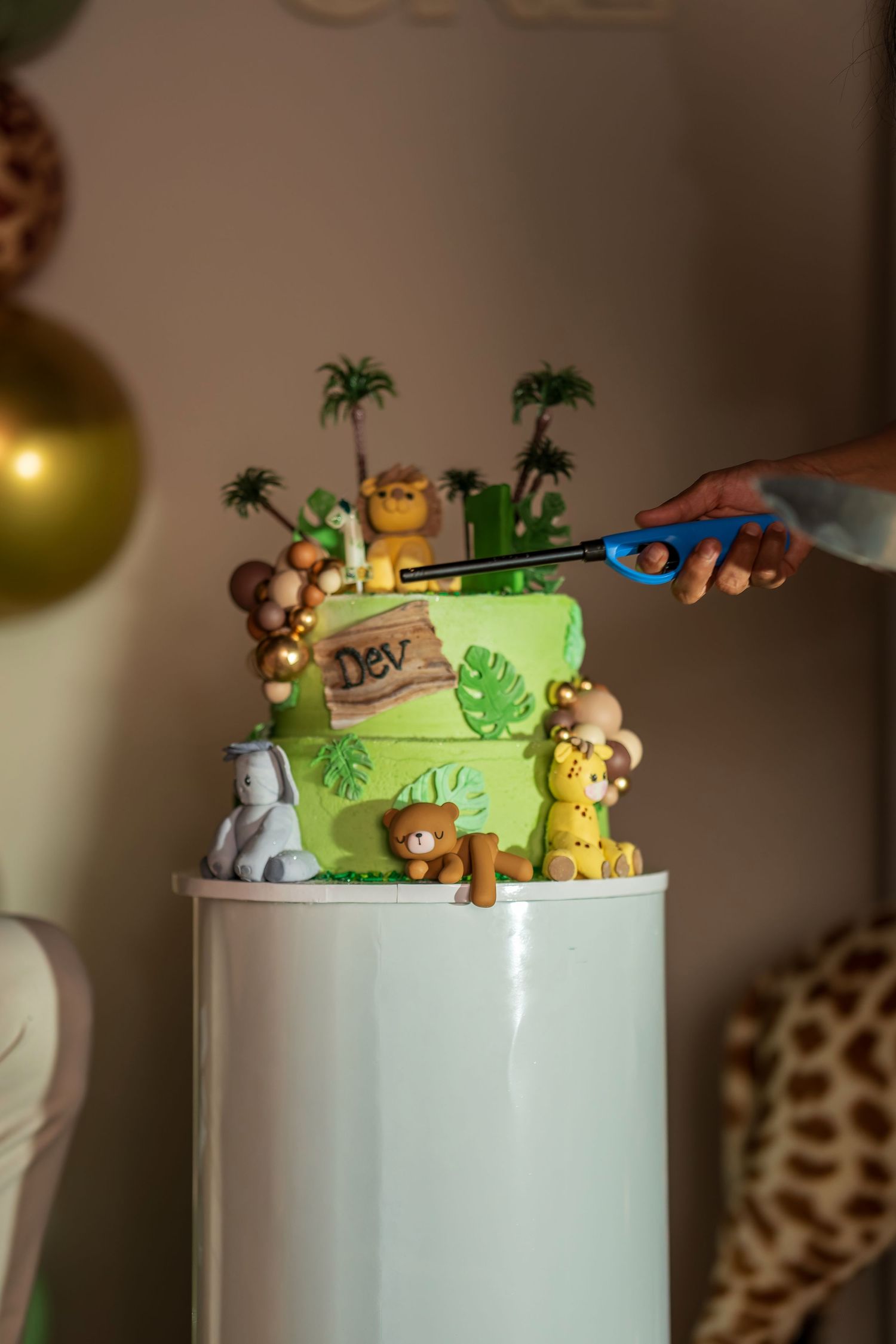 A safari-themed birthday cake decorated with palm trees and animal figures sits on a white pedestal.
