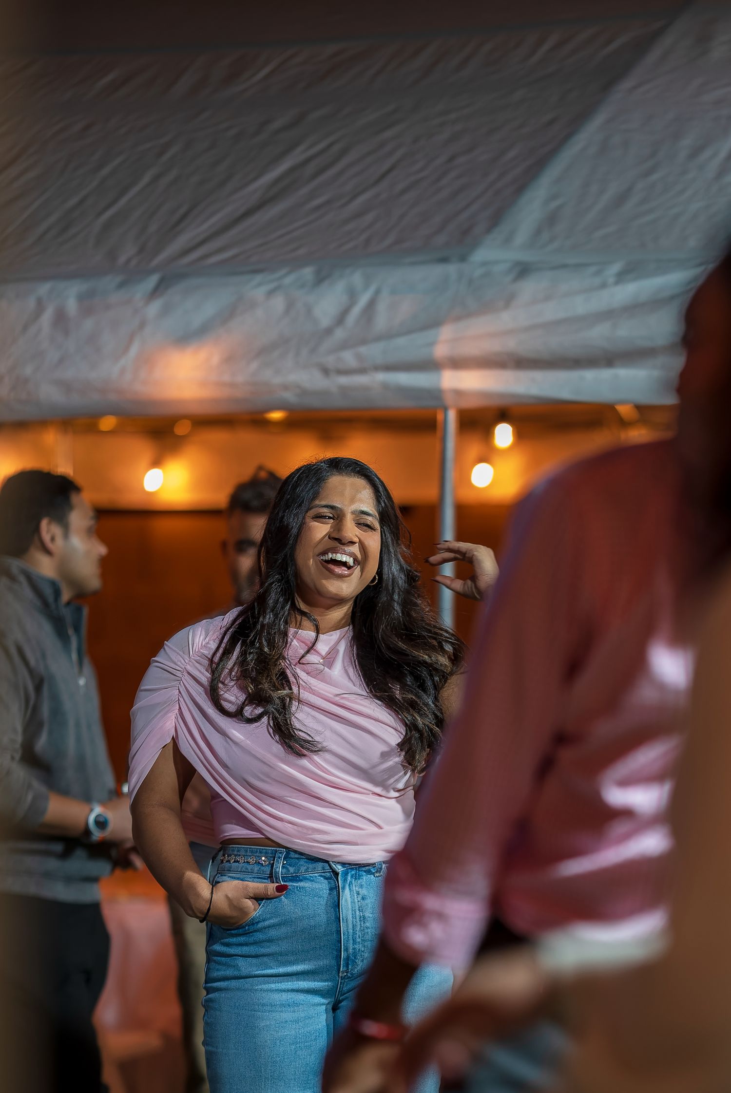 Someone wearing a pink top and jeans dances joyfully under party lights.