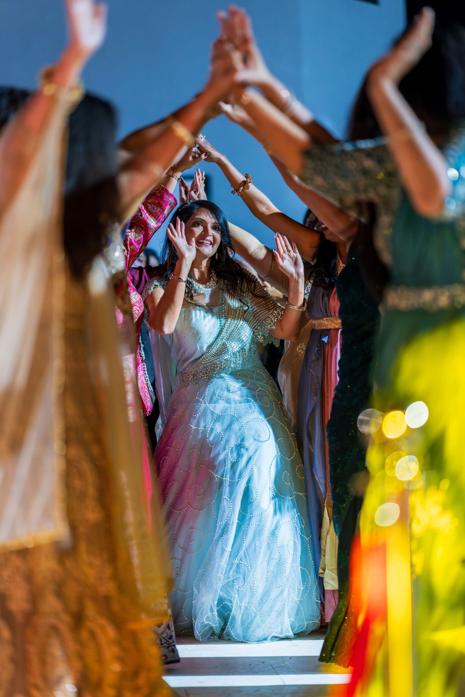 A performer in a light blue dress raises their arms joyfully during a dance number with colorful lighting.