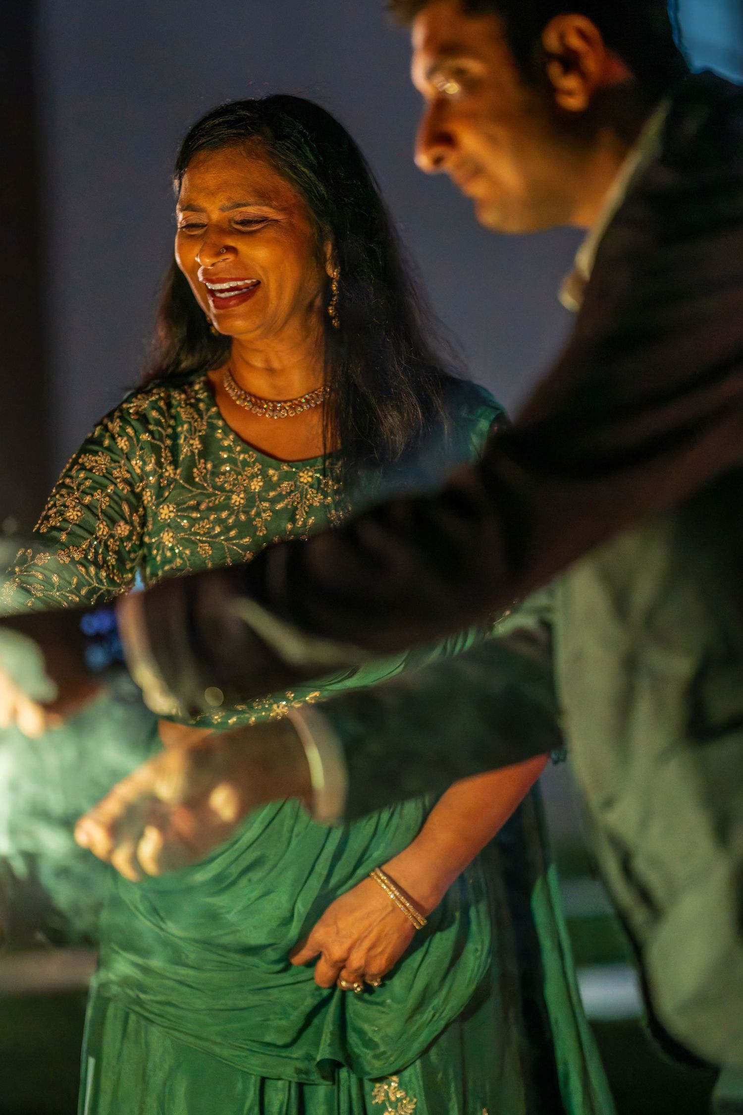 A woman in a green traditional outfit laughs and dances during a festive celebration.